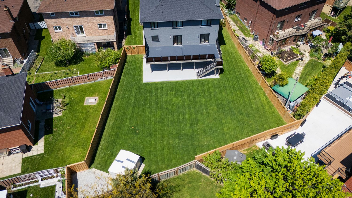 Aerial drone view of suburban neighborhood with green lawns, houses, and trees on a sunny day.