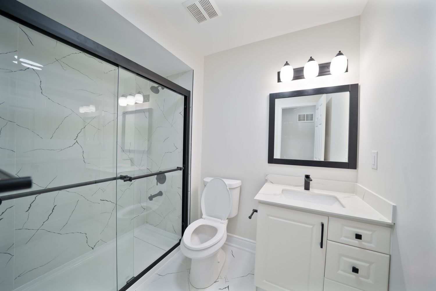 Modern white marble bathroom features sleek glass shower enclosure and contemporary fixtures with clean lines.