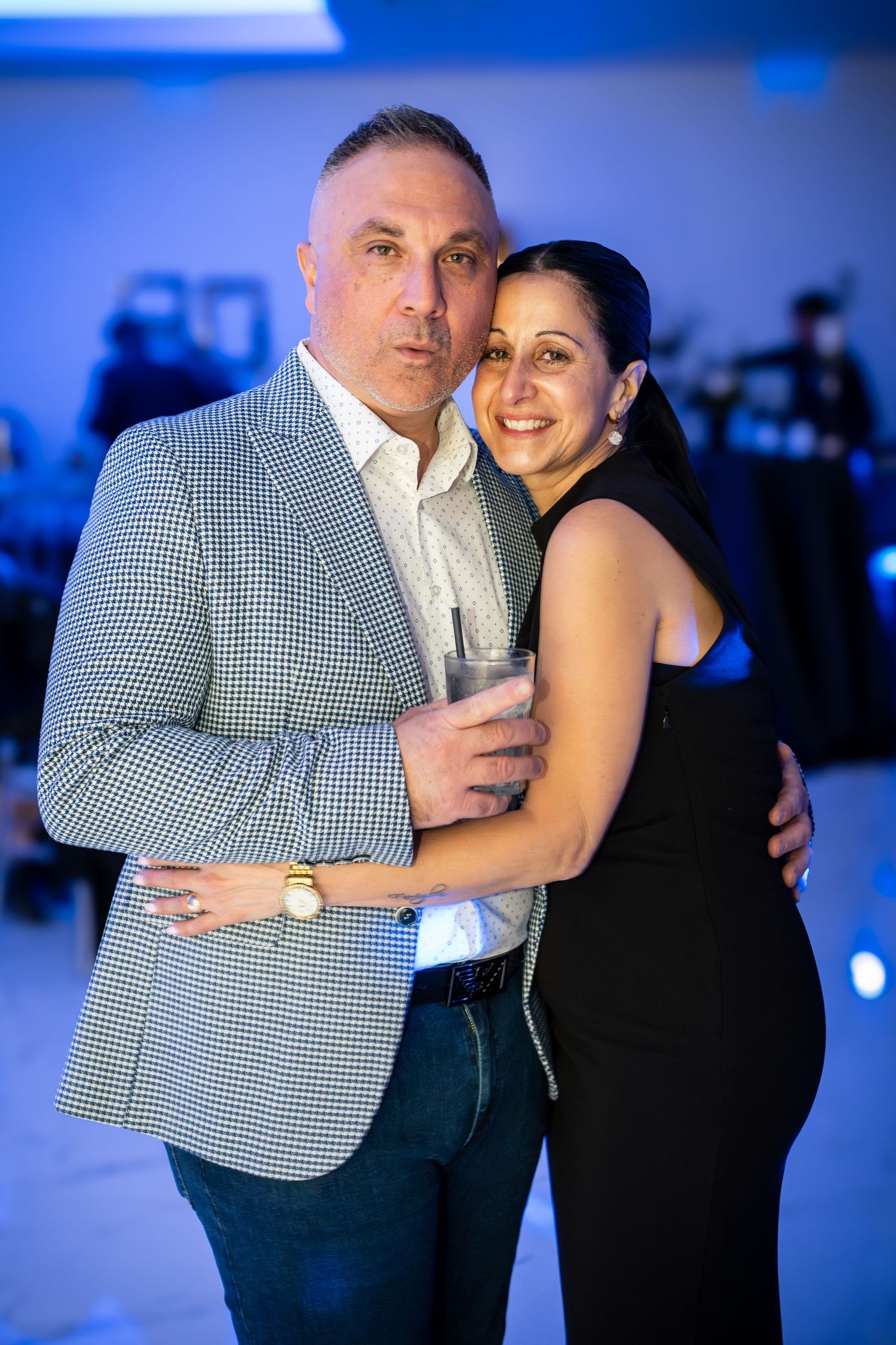A couple embraces while posing for a photo at an evening event with blue lighting.