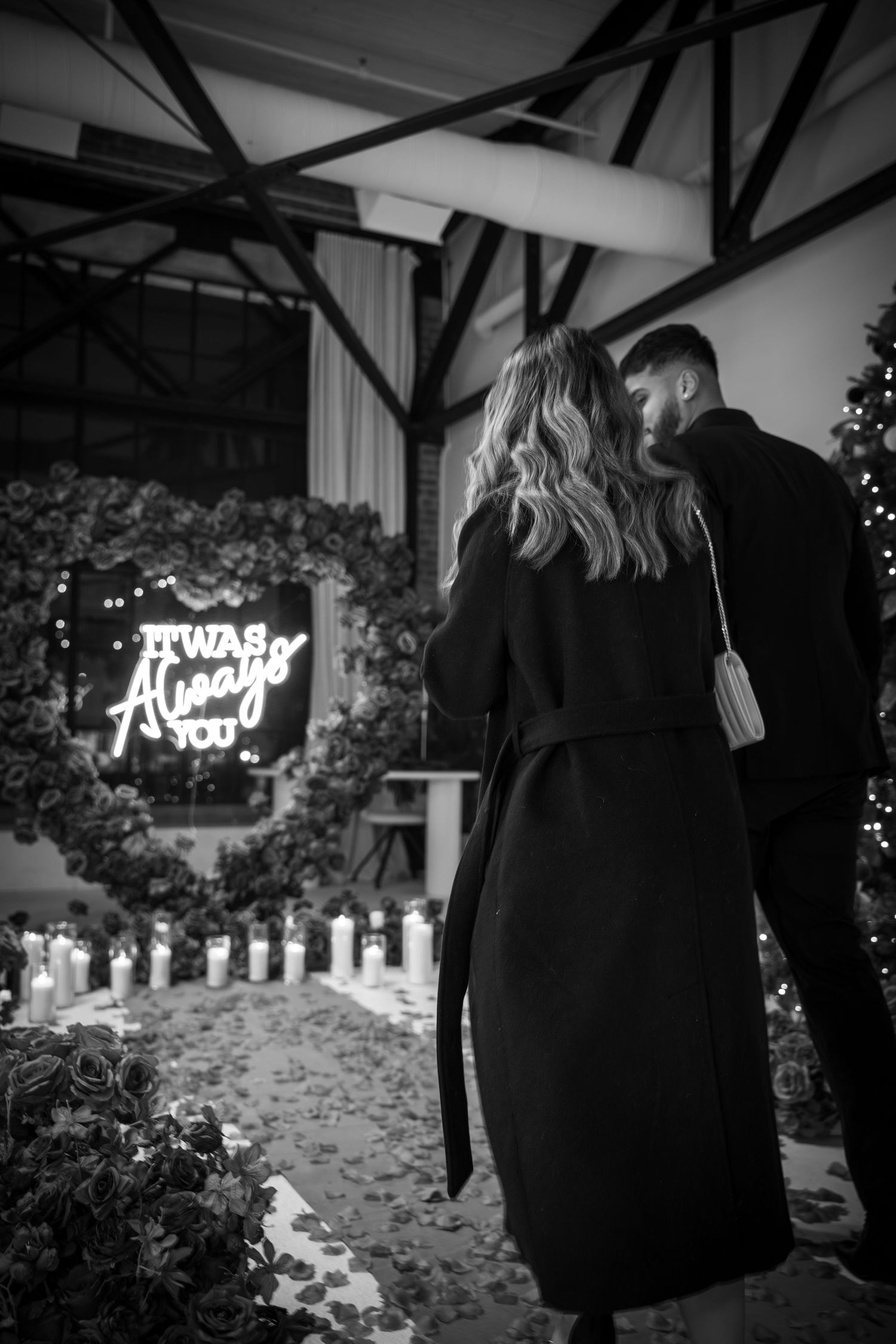 A romantic proposal setup with neon signage and floral decorations in black and white.