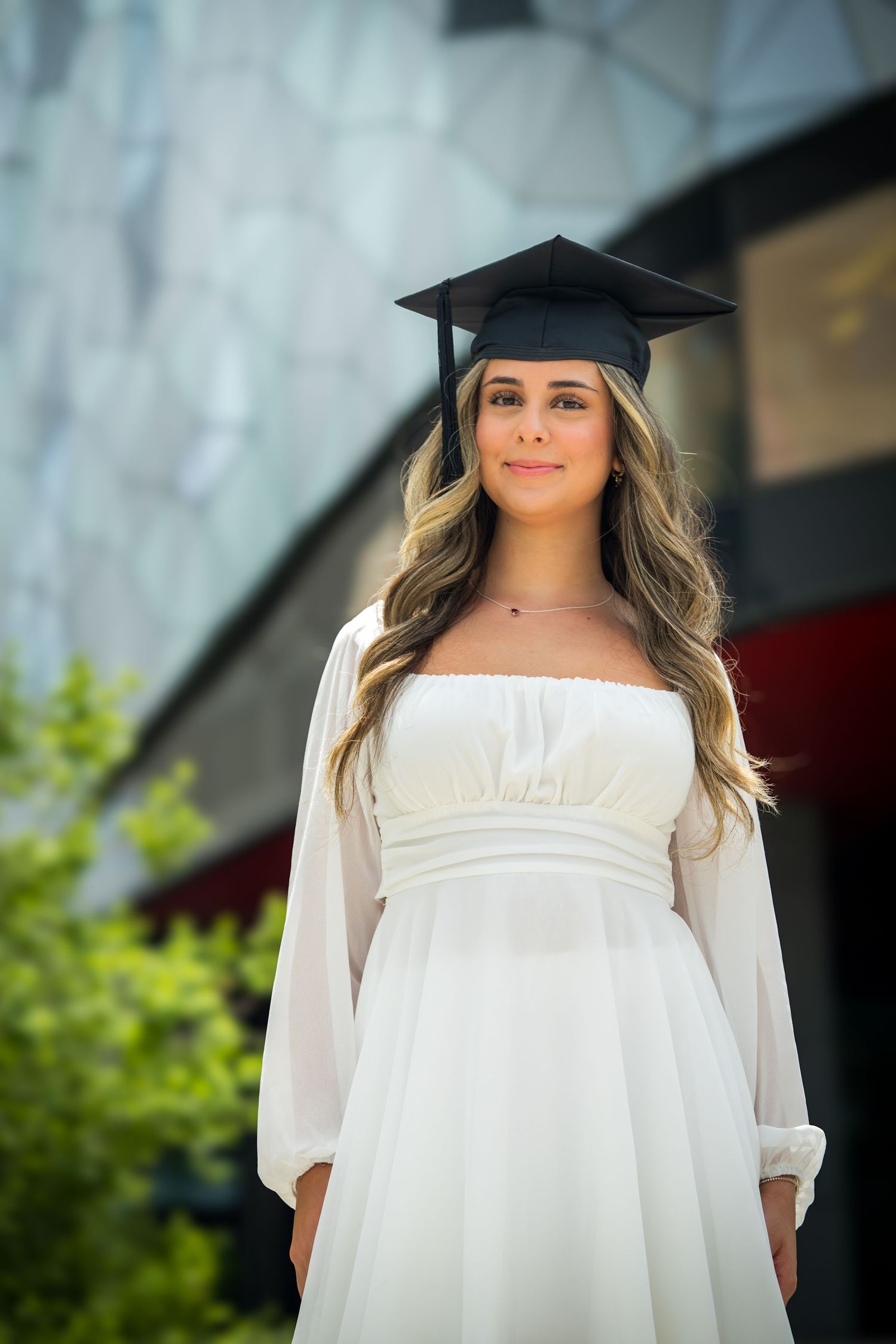 Graduate in elegant white dress poses for commemorative photos outdoors.