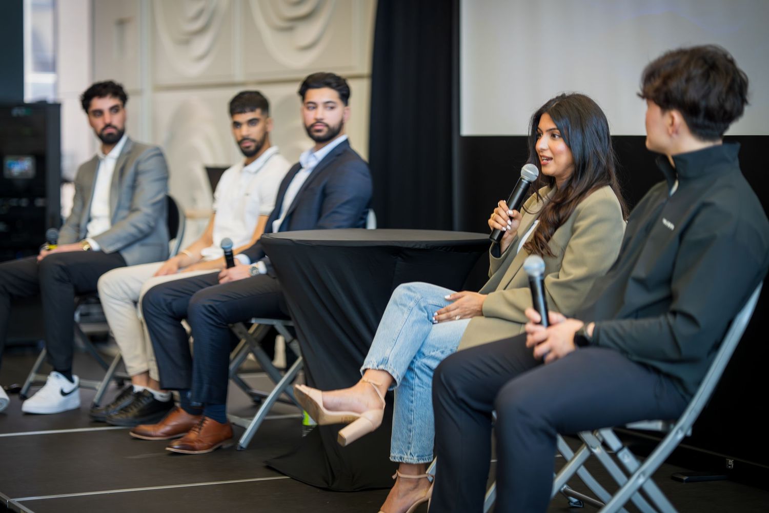 Wide shot of panel discussion showing five speakers seated on stage with microphones.