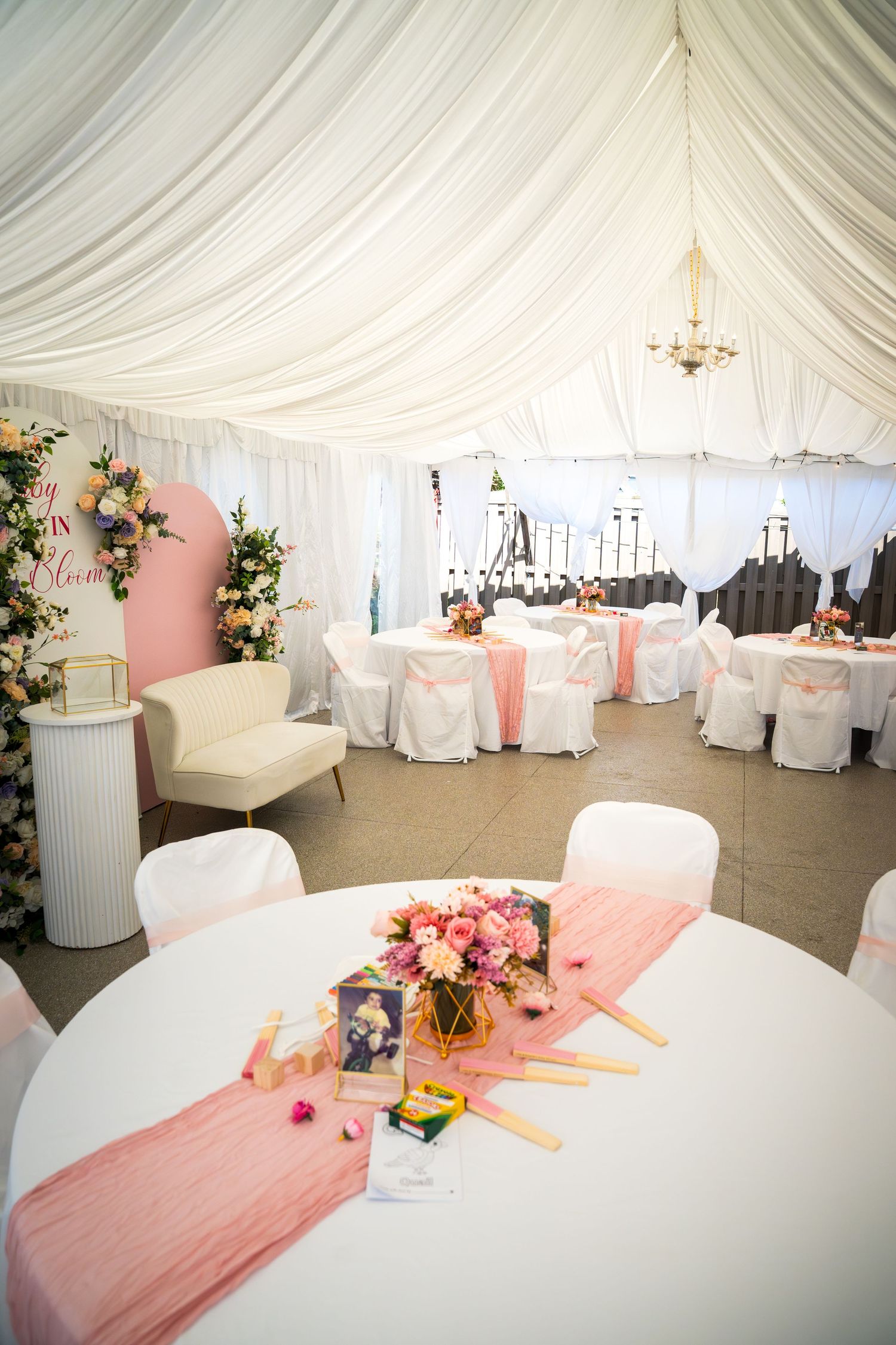 Wedding reception setup with white chairs and pink table runners under draped tent ceiling.