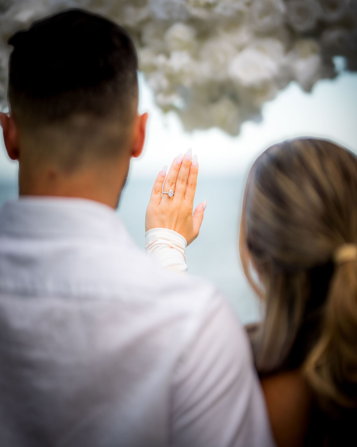 Close-up shot of a hand showing off an engagement ring against a blurred background.