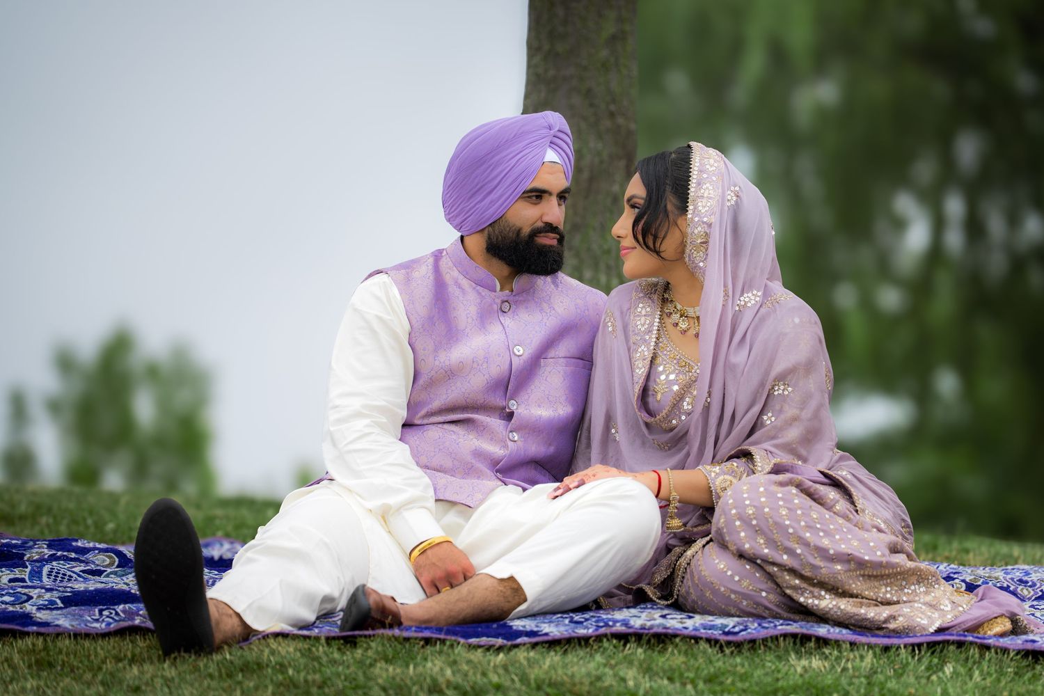 Three people in coordinated traditional outfits lounge together on a patterned blue blanket in a park.