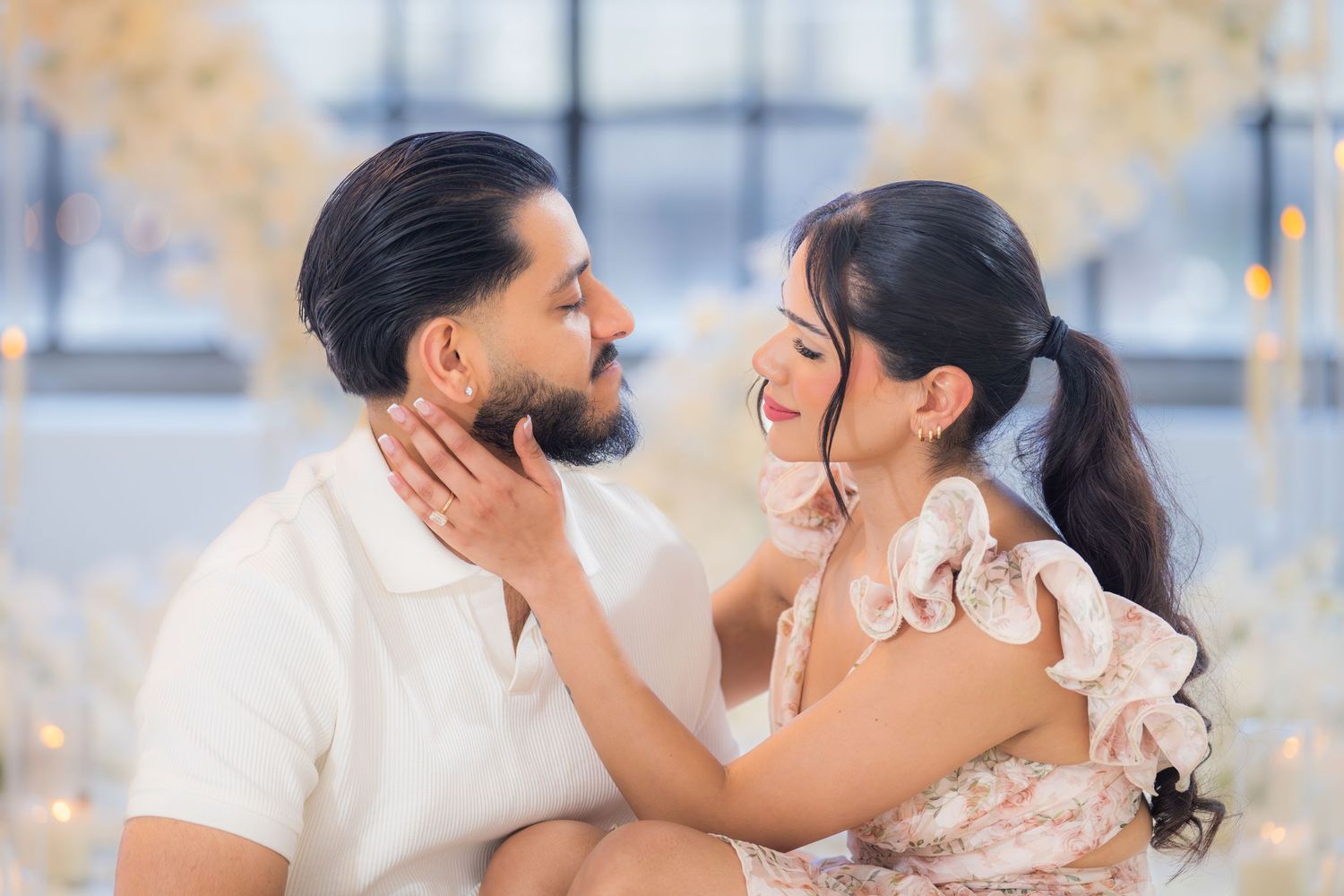 Close-up of a couple gazing lovingly at each other surrounded by elegant white floral decorations and soft lighting.