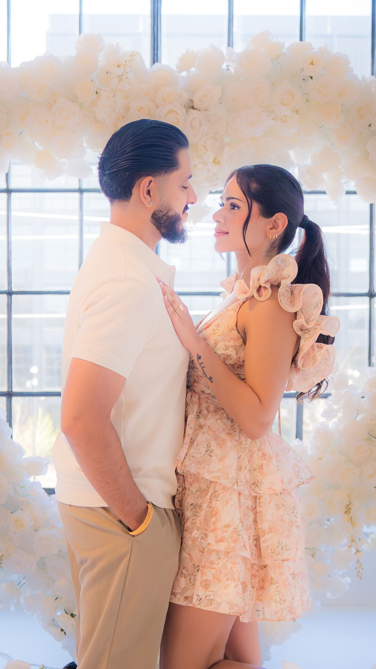 Couple gazes into each other eyes in front of a lush white floral arrangement in a bright studio.