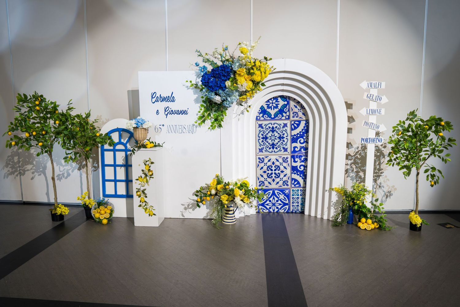 Elegant wedding backdrop with blue and white arch, decorative tiles, yellow and blue flowers, and lush green trees.