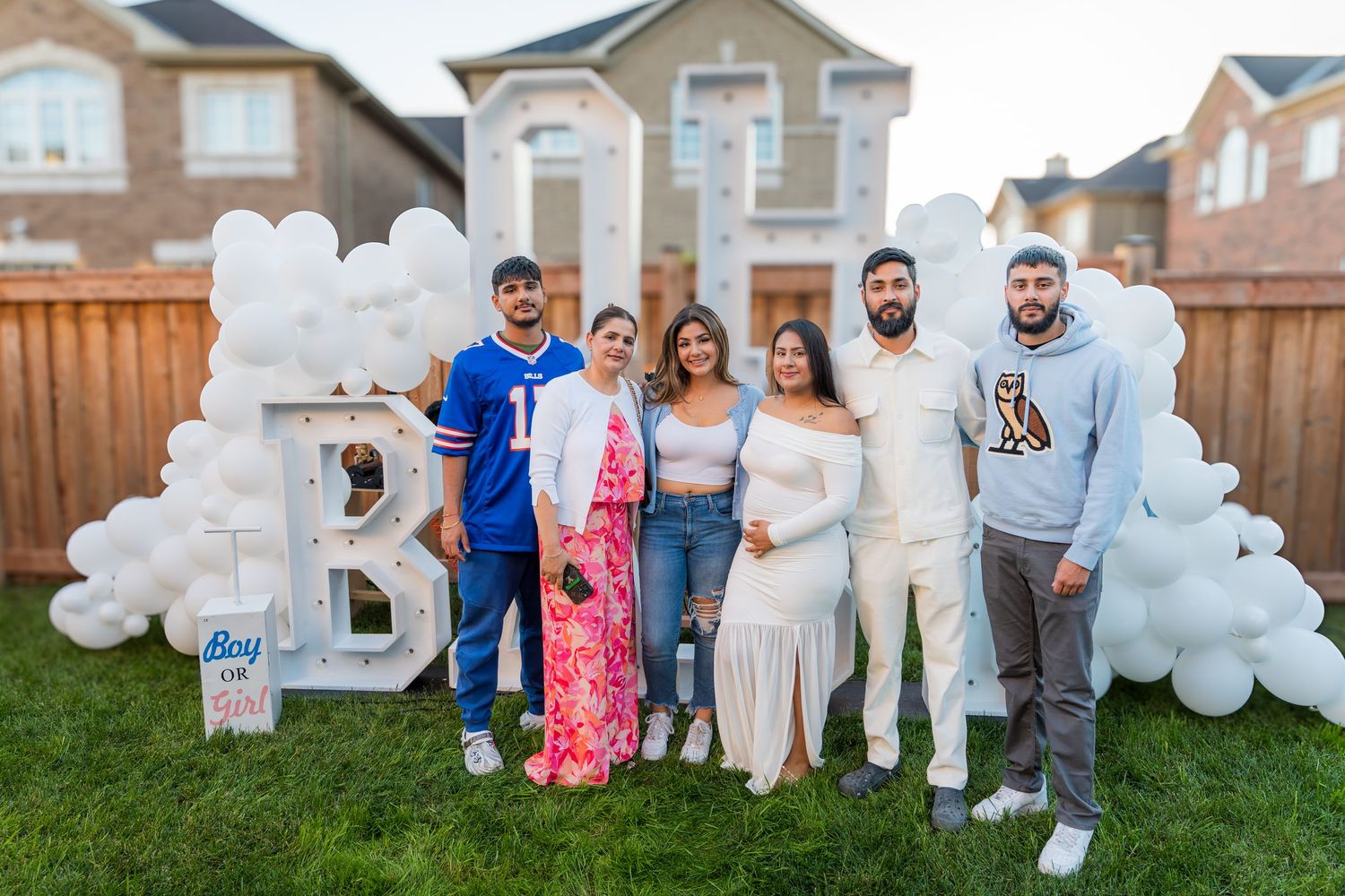 Group of six people posing outdoors at a baby shower with white balloon decorations spelling BOY.