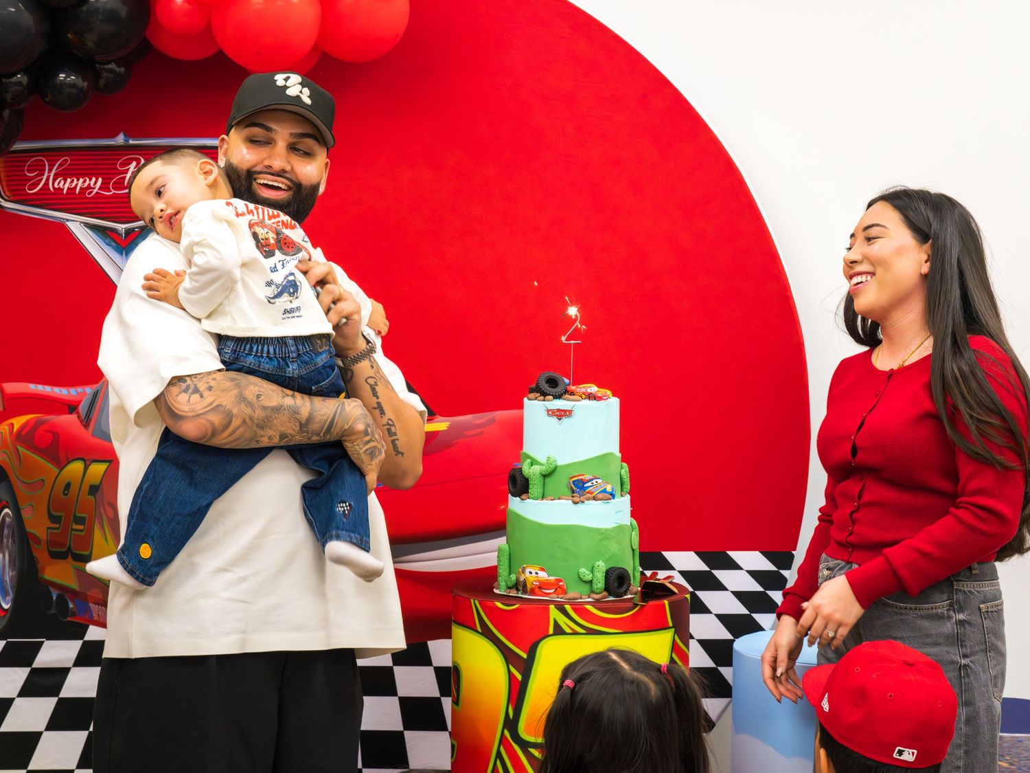 Family celebrating child birthday party with Cars-themed cake and decorations.