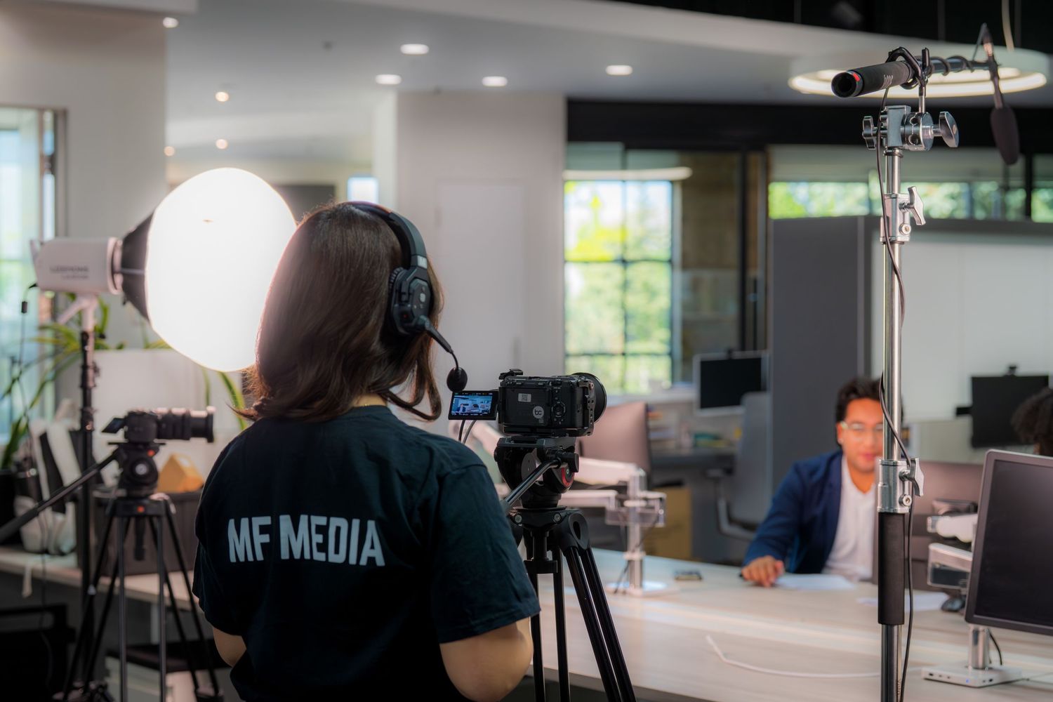 MF Media videographer filming a corporate interview with professional lighting equipment in a modern office.