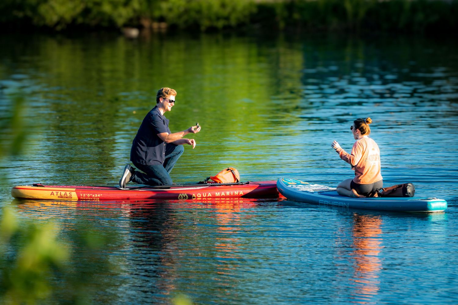 Two people on colorful paddleboards on a calm green lake on a sunny day.