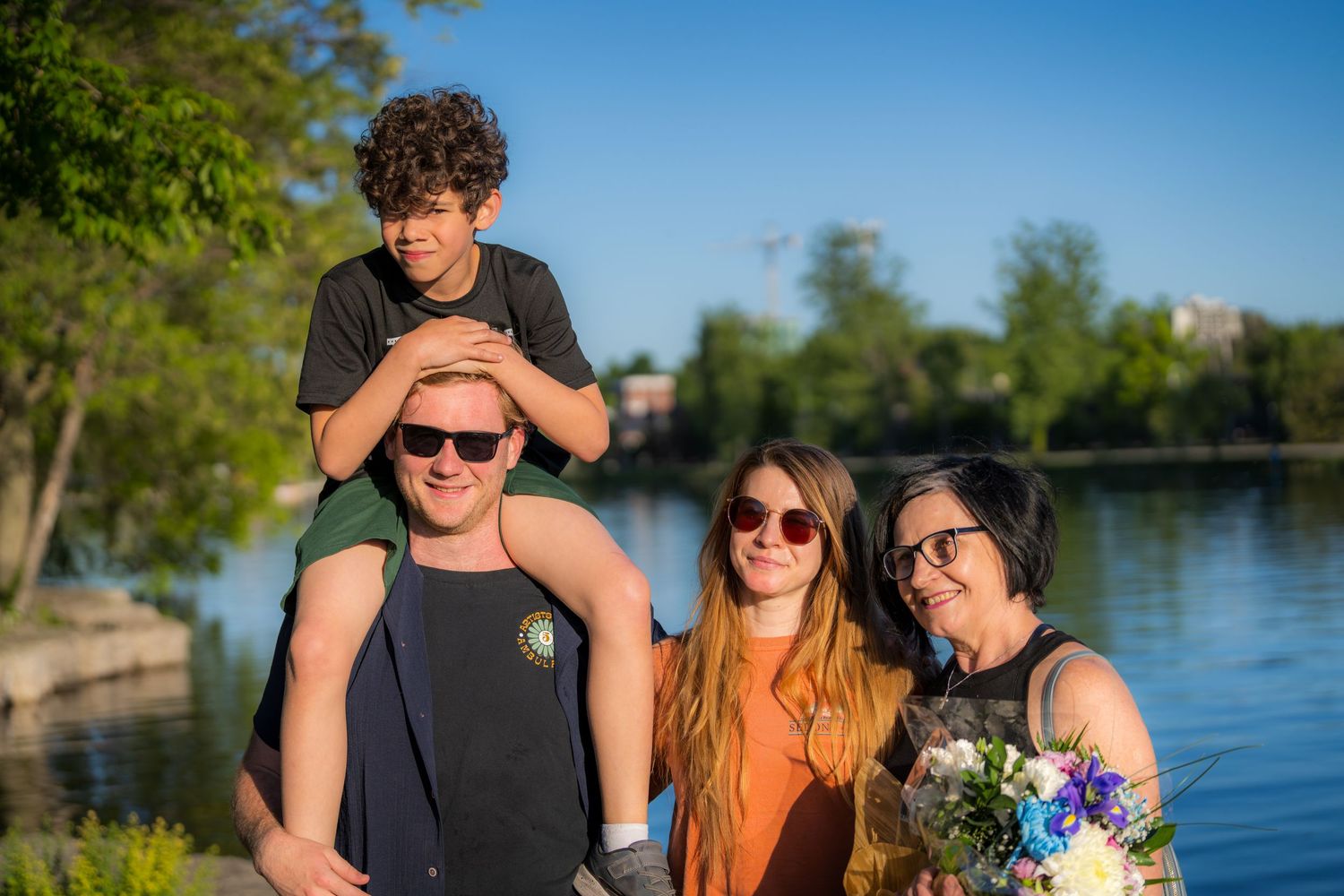 Happy family of four posing together by a sunny lakeside park.