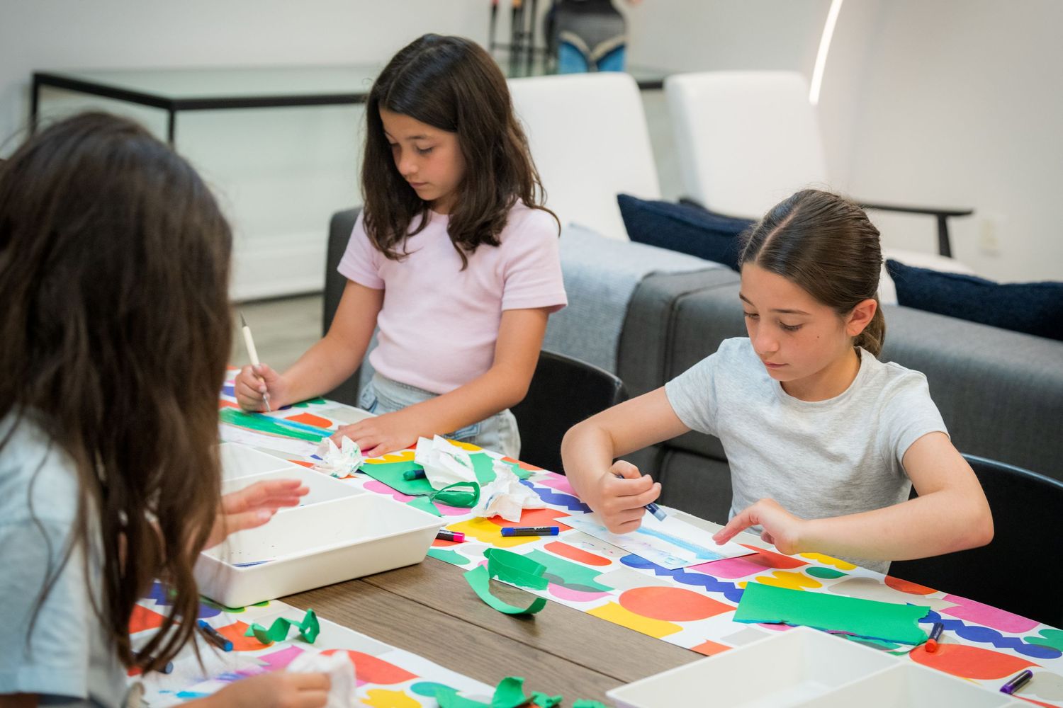 Children collaborate on vibrant paper collage artwork at a colorful table during an art workshop.