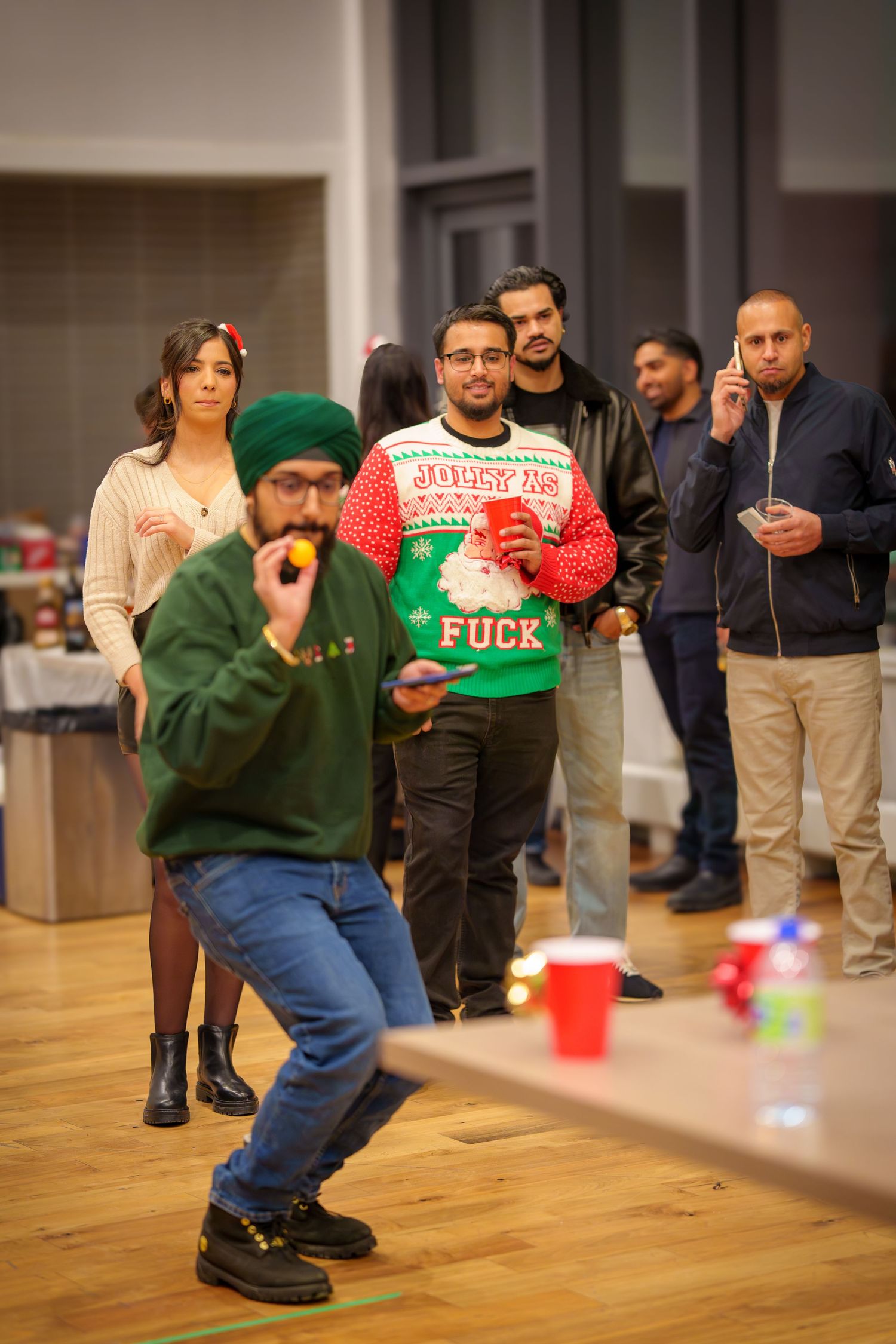 People playing party games at an indoor gathering with someone wearing a festive holiday sweater.
