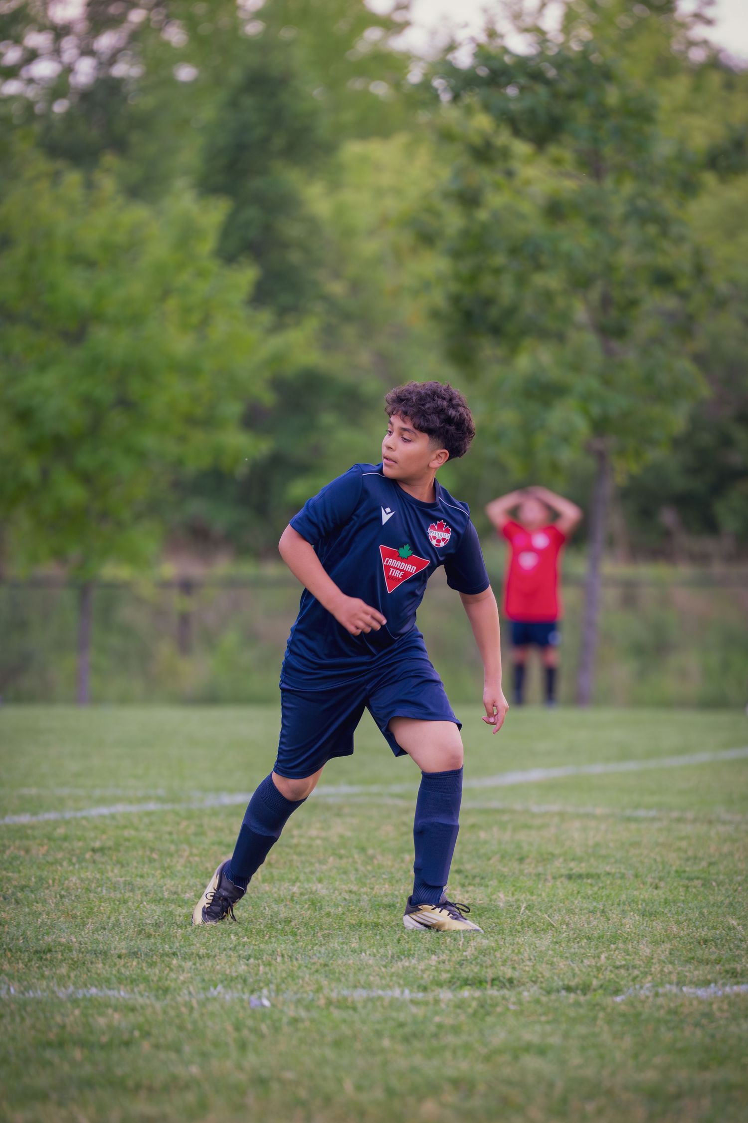 A youth soccer player in a navy blue uniform practices stretching exercises on a grassy field.
