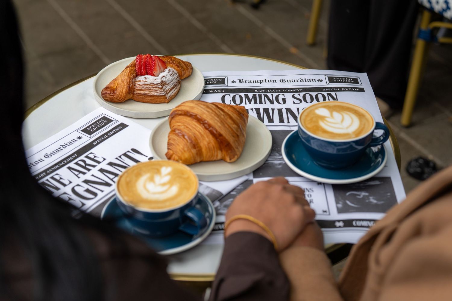 A coffee cup with latte art sits next to a croissant on a white plate at a cafe table.