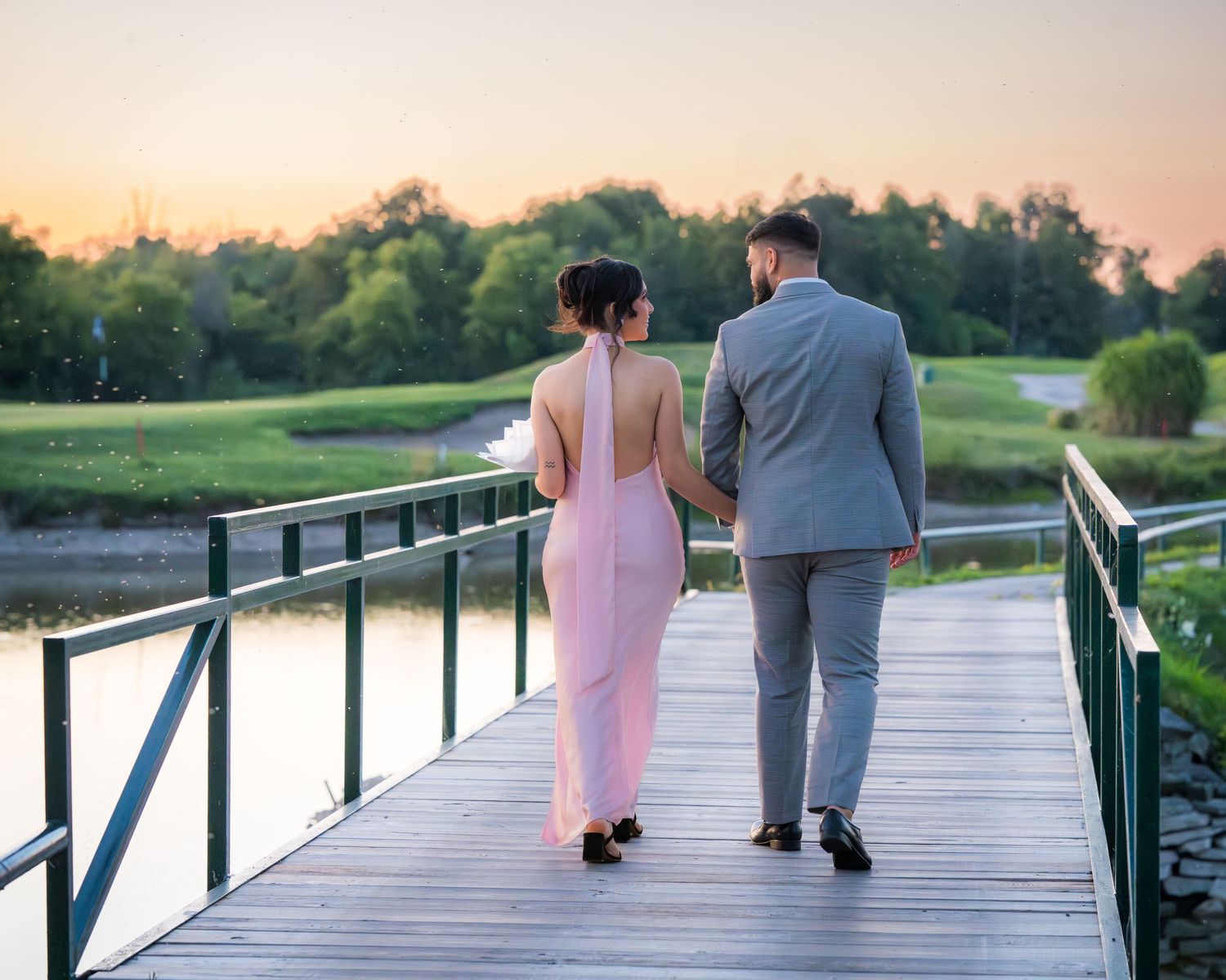 Two people walking away on a wooden bridge over water during sunset.