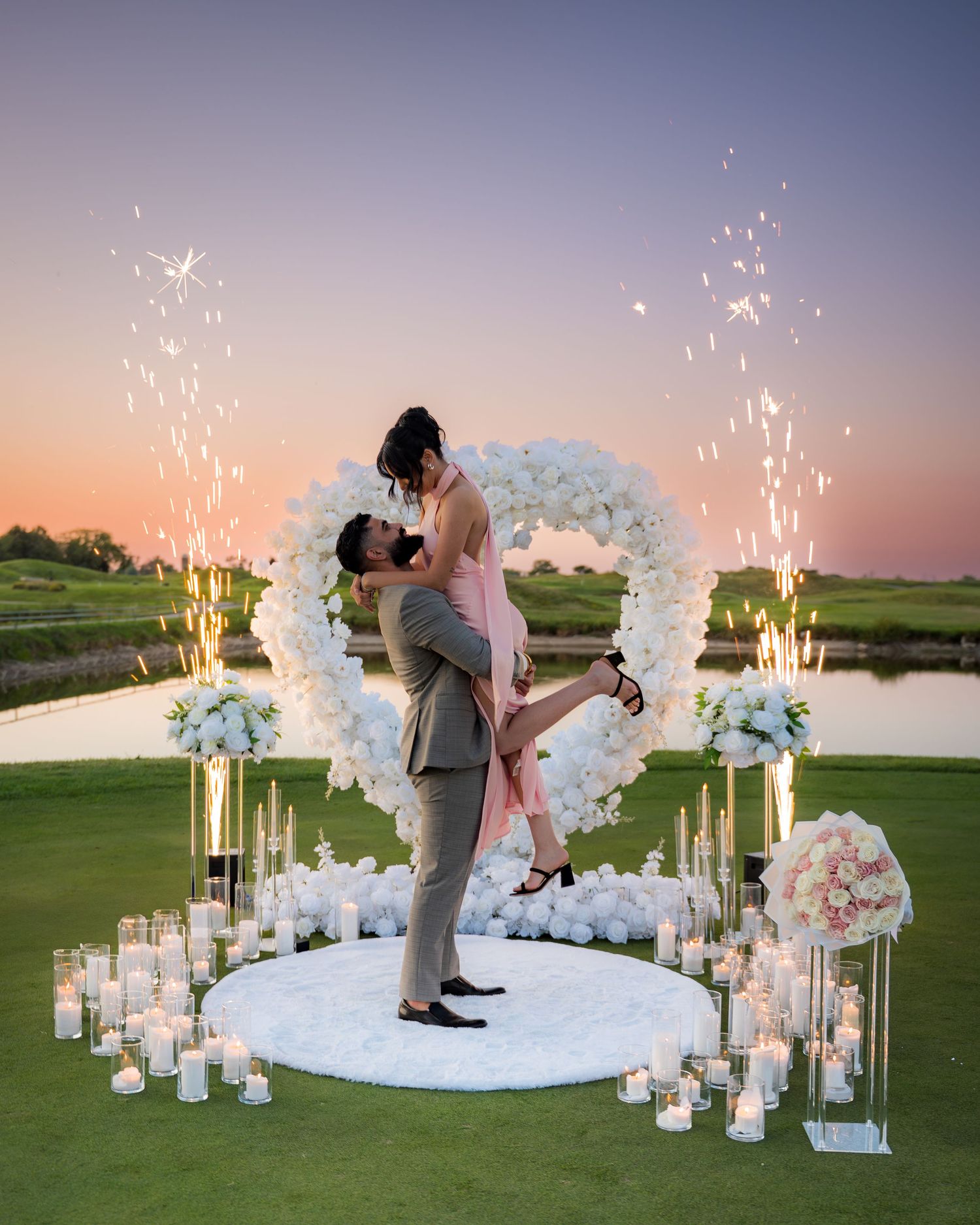Romantic proposal celebration with sparklers and floral decorations at sunset.