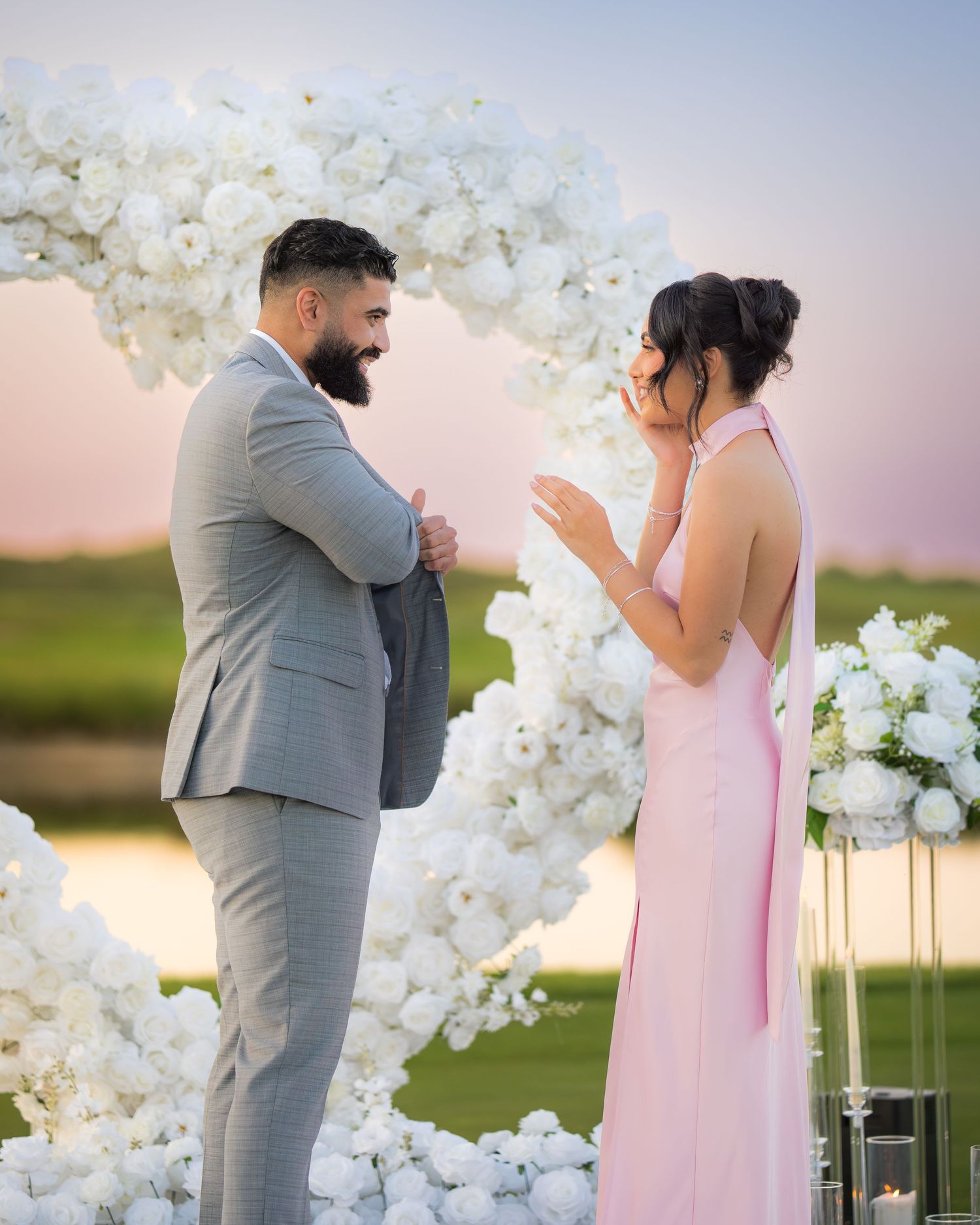 Romantic lakeside proposal featuring an ornate white flower arch and glowing candle arrangements.