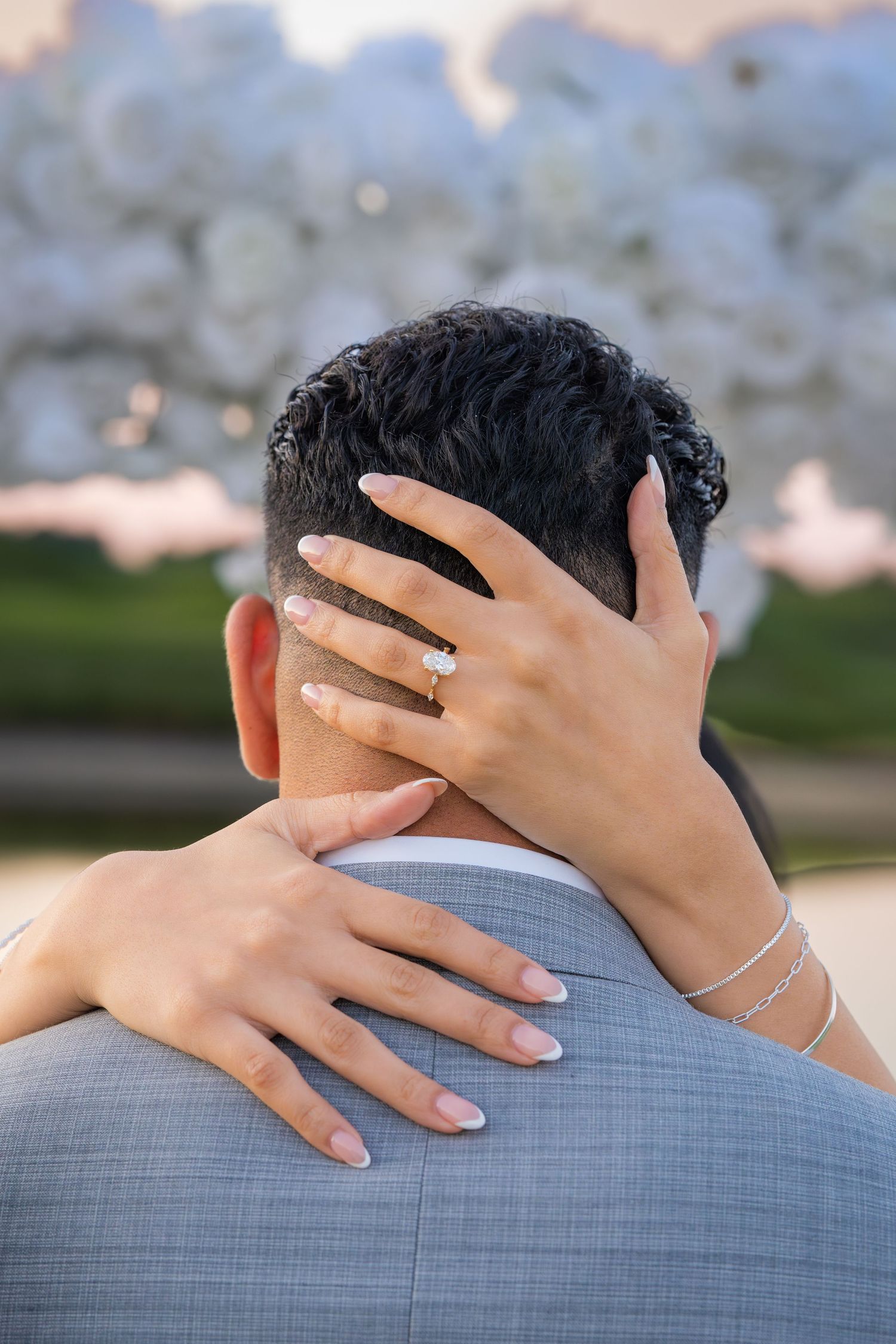 Hands resting on grey suit jacket showing wedding rings during sunset photoshoot.