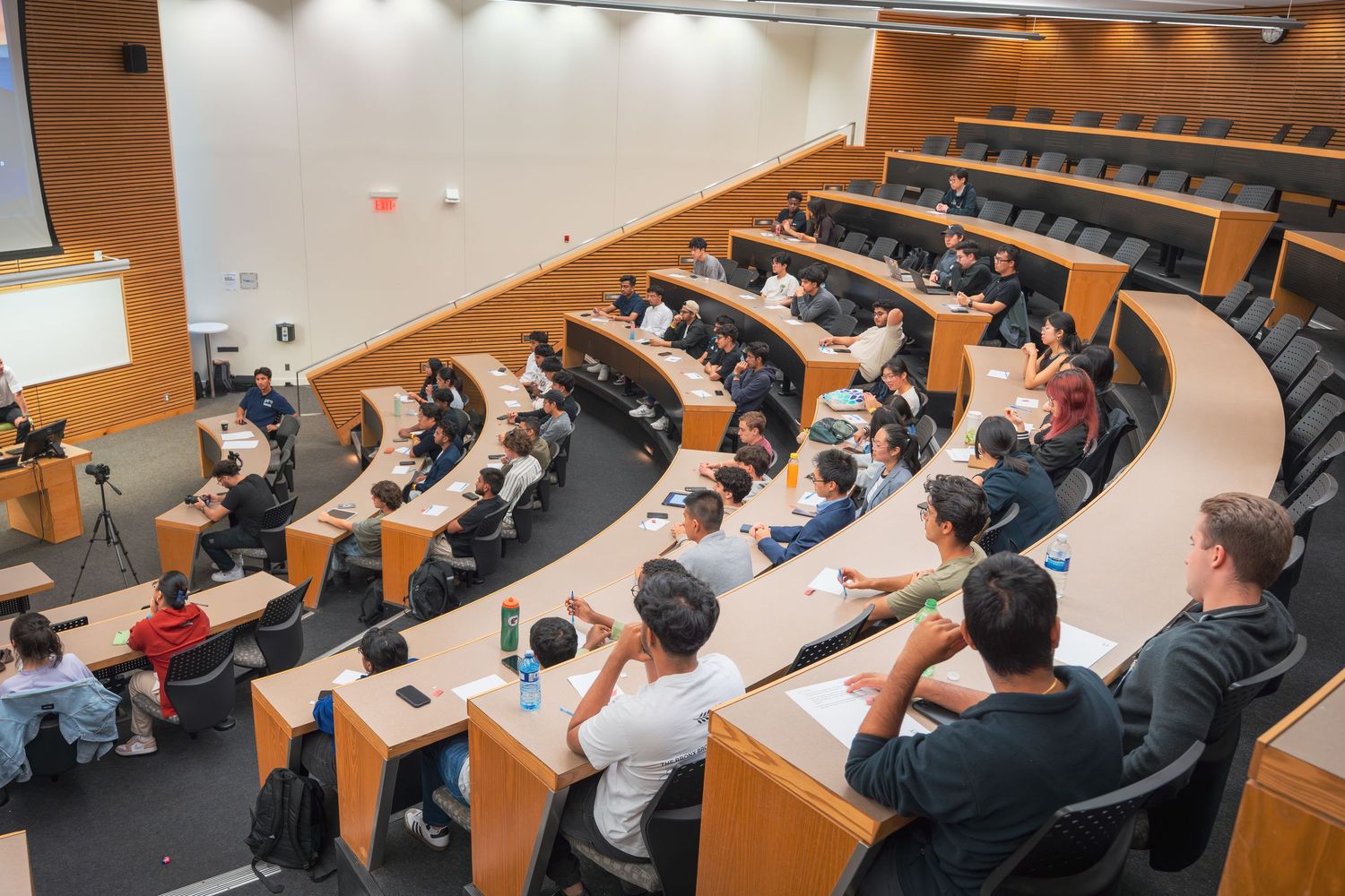 Wide view of an auditorium filled with attendees watching a presentation in stadium-style seating.