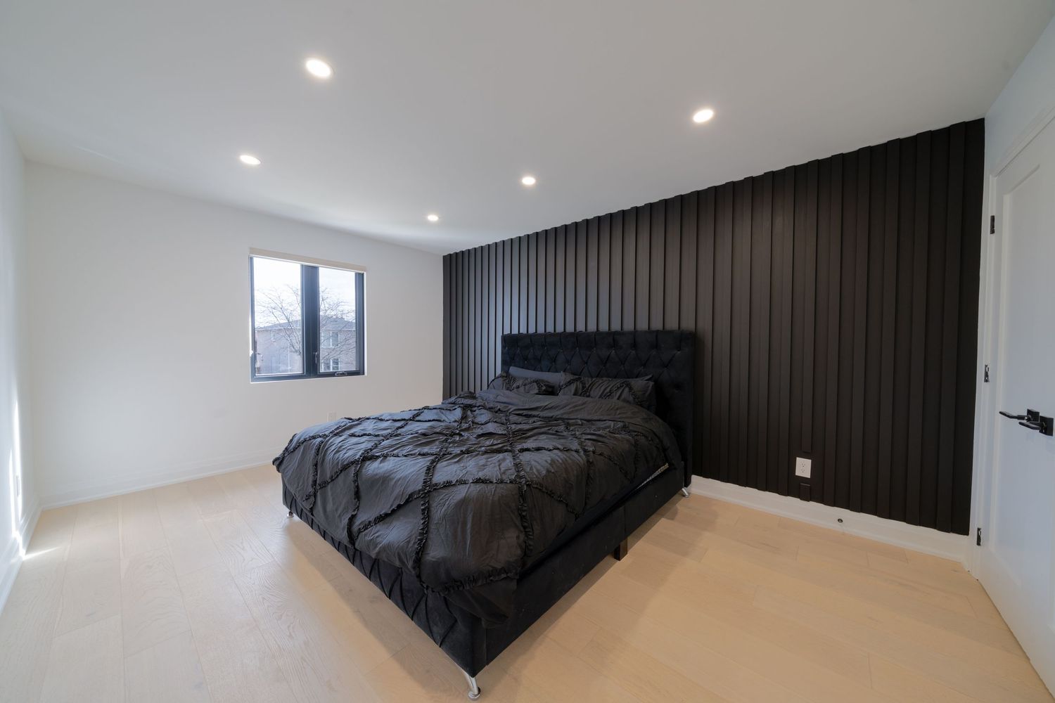 Modern bedroom interior with recessed lighting, dark accent wall, and large windows providing natural illumination.