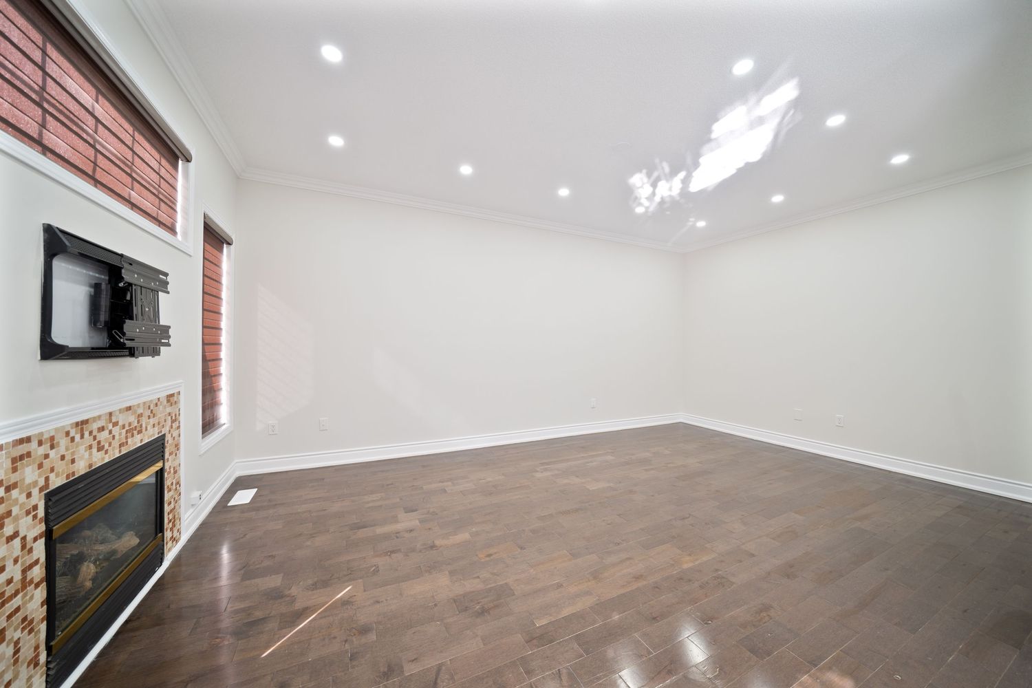 Modern open concept living room with white walls, recessed lighting, and hardwood flooring in a residential space.