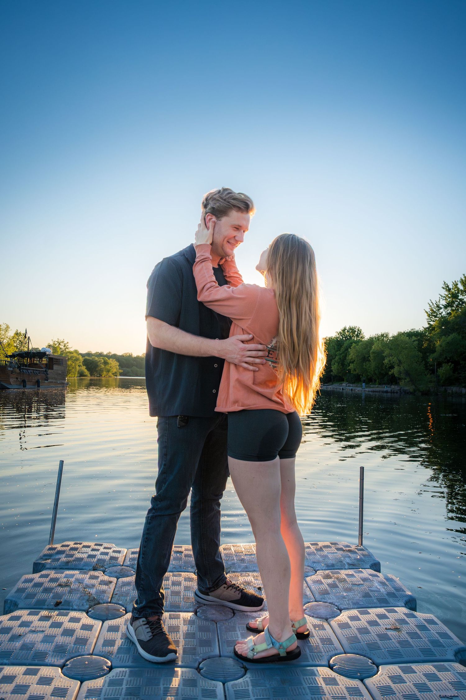 Young couple embracing on a floating dock at golden hour with a calm lake in the background.