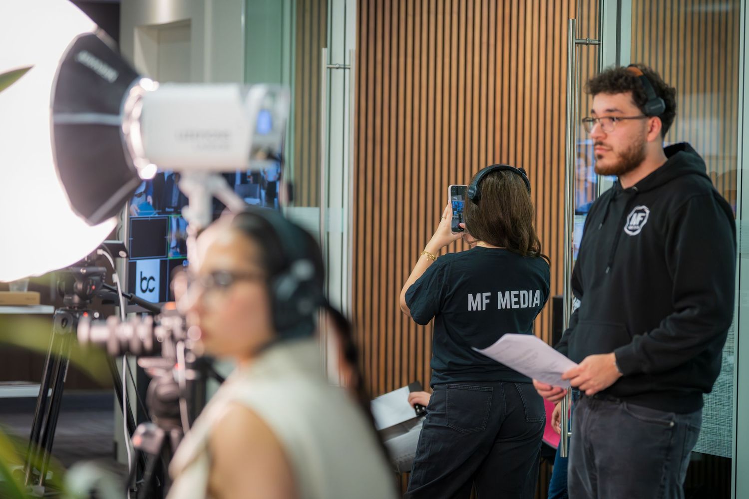 MF Media crew filming on set with professional lighting equipment and camera in a modern studio.