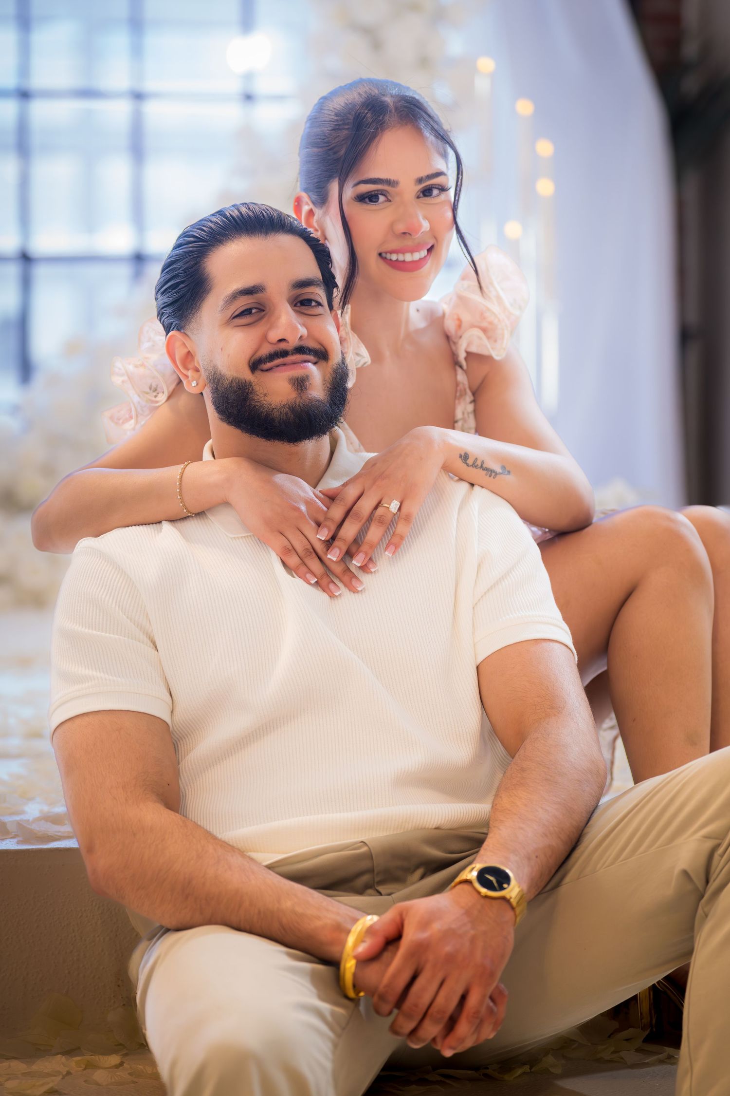 Engaged couple posing together, woman draping arms over mans shoulders showing engagement ring.