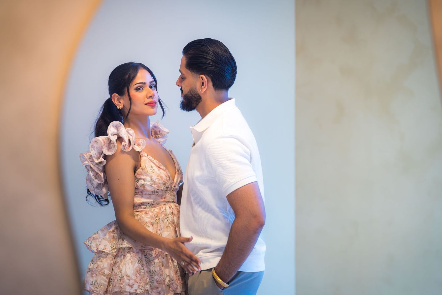 Couple gazing at each other romantically in front of arched mirror in bright room.