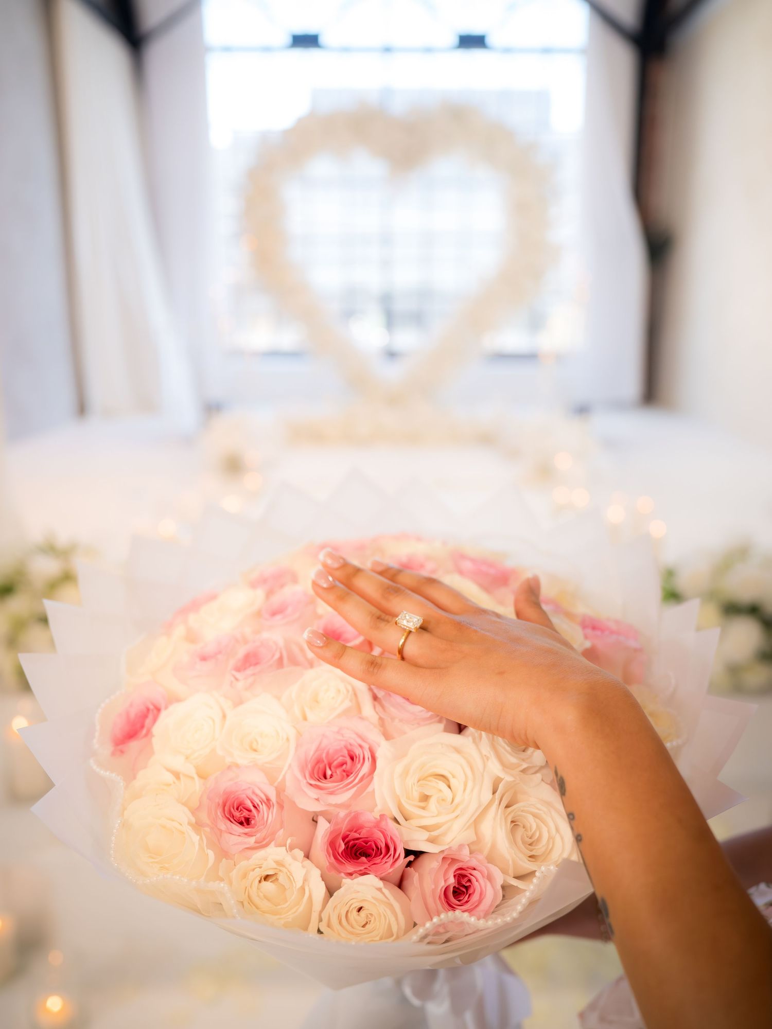 Hand with diamond engagement ring resting on pink and white rose bouquet at romantic proposal venue.