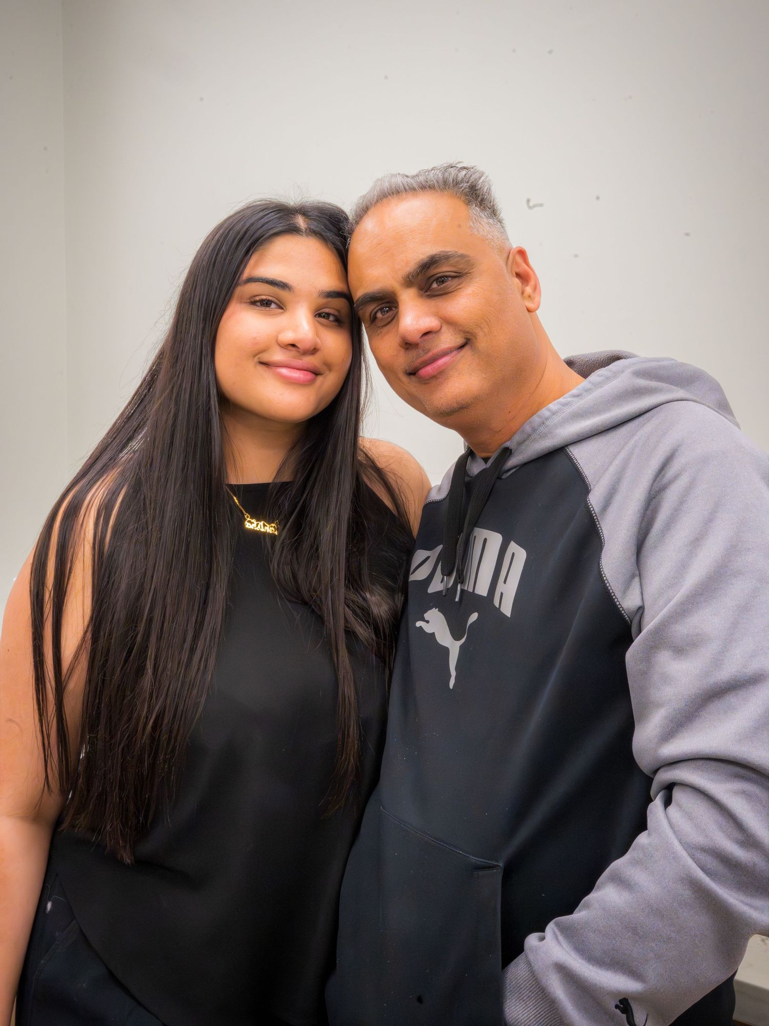 A young woman and middle-aged man smiling together, wearing casual black and gray Puma outfits against a white wall.