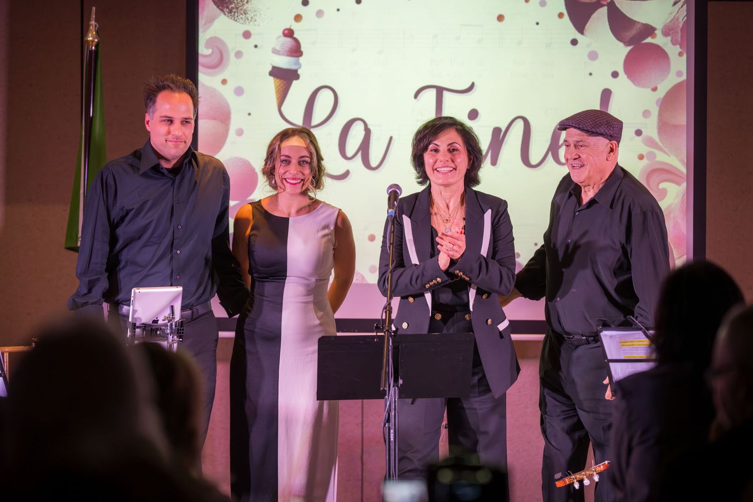 Four performers take a bow on stage in front of a La Fine projection screen at event finale.