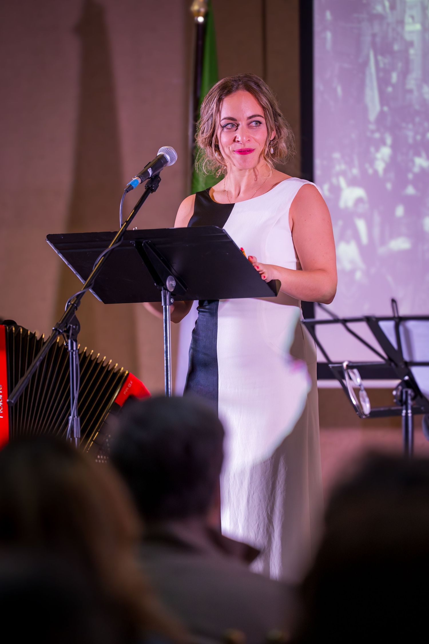 Woman in black and white sleeveless dress speaking at a podium microphone during a formal evening ceremony.
