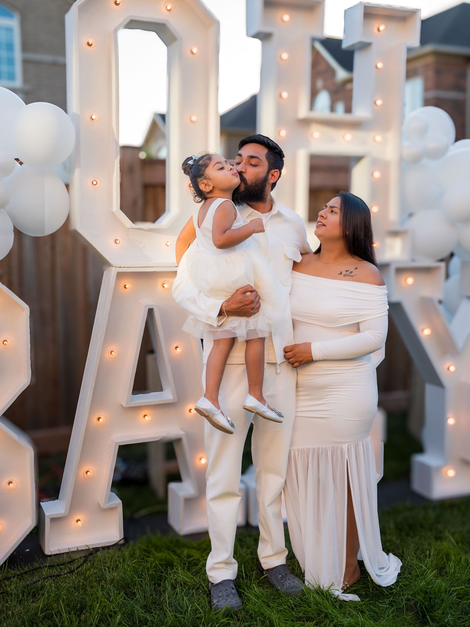 Family posing at an OH BABY gender reveal party with illuminated marquee letters and white balloon decorations.