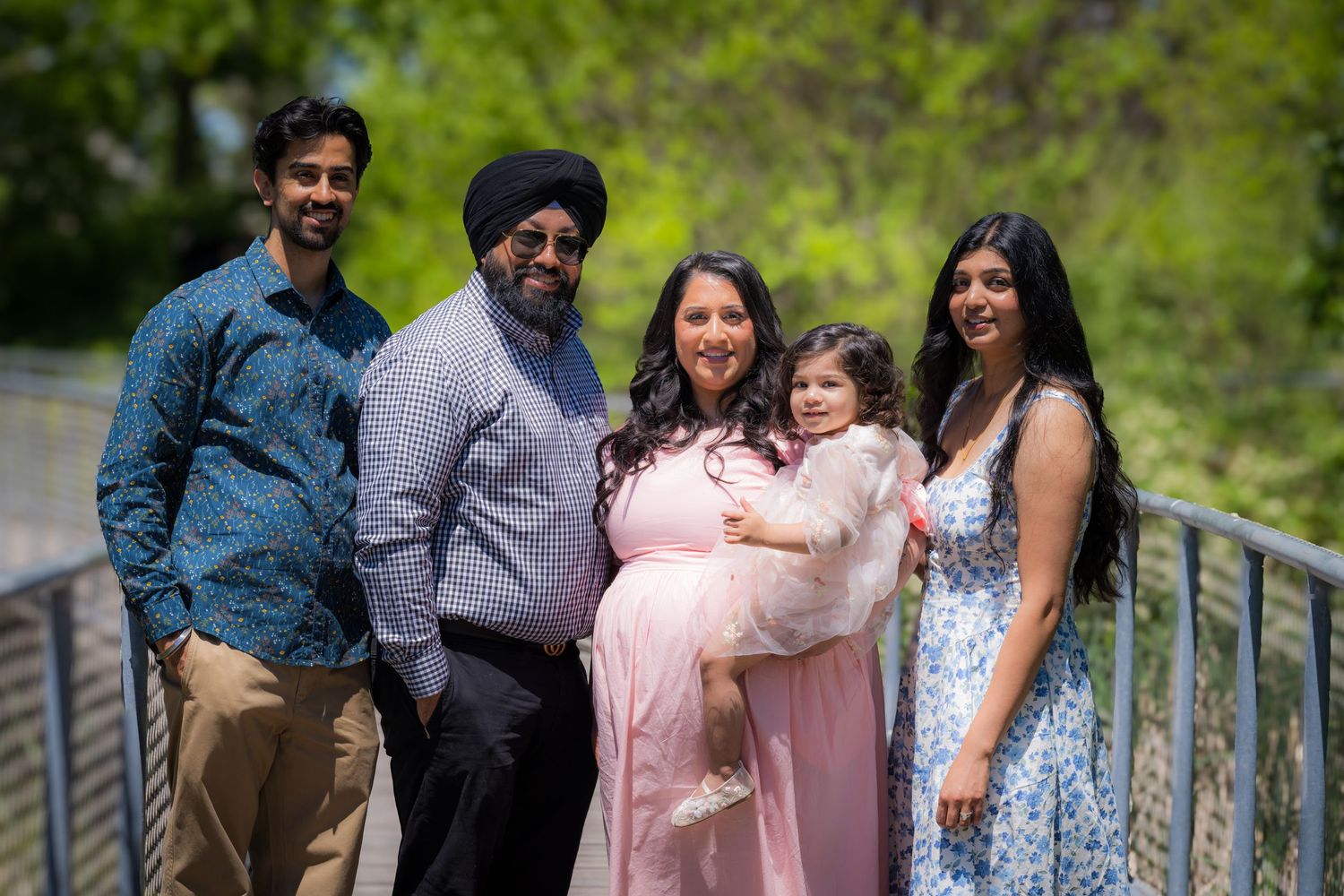 A South Asian family of five poses on a bridge, with a pregnant woman in pink holding a young child.