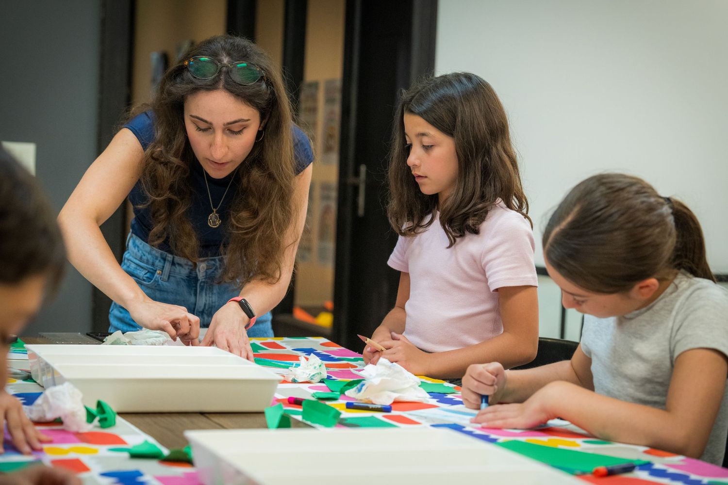Female art teacher guides children through colorful paper collage project at creative kids workshop.