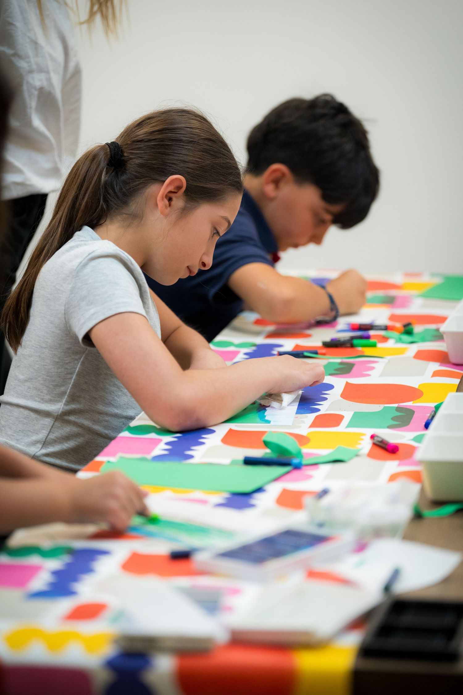 Young girl focuses on creating a colorful paper collage artwork during a kids art class.