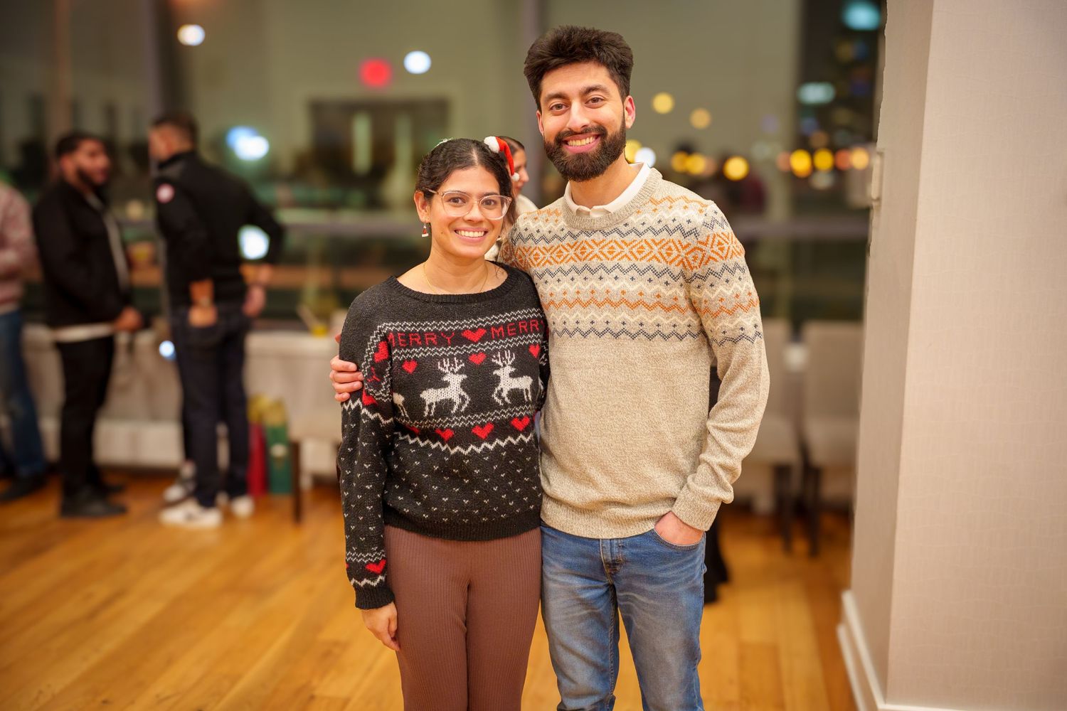Group of people wearing cozy winter sweaters at an indoor holiday gathering.