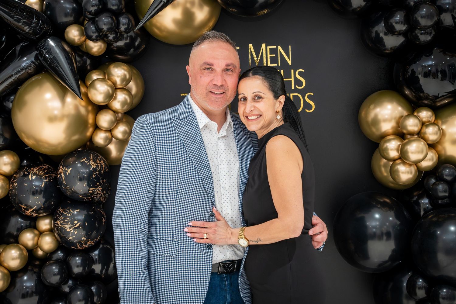 Guests posing for photos at formal event with black and gold balloon wall backdrop.