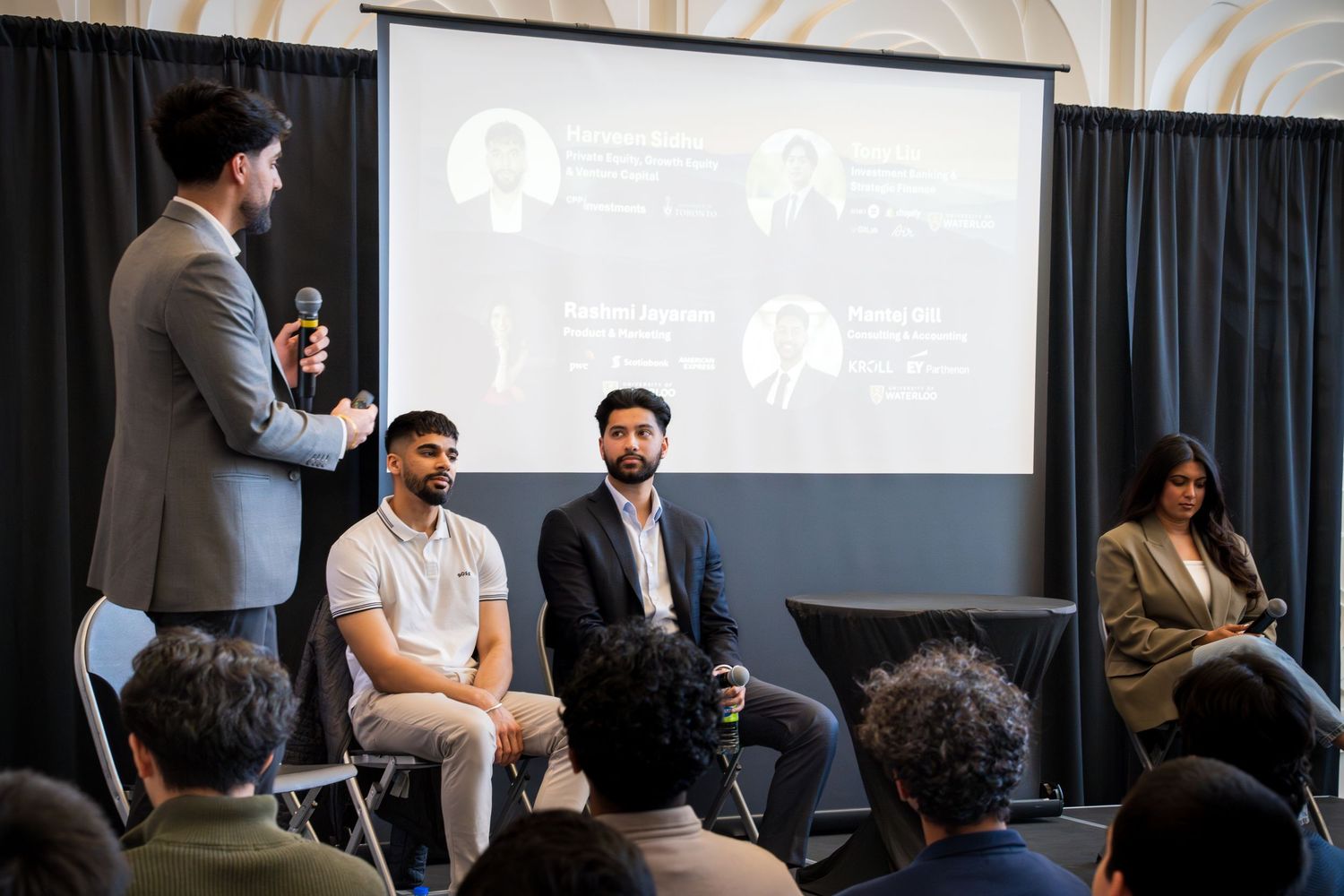 Wide shot of panel discussion with speakers and audience in contemporary conference setting.