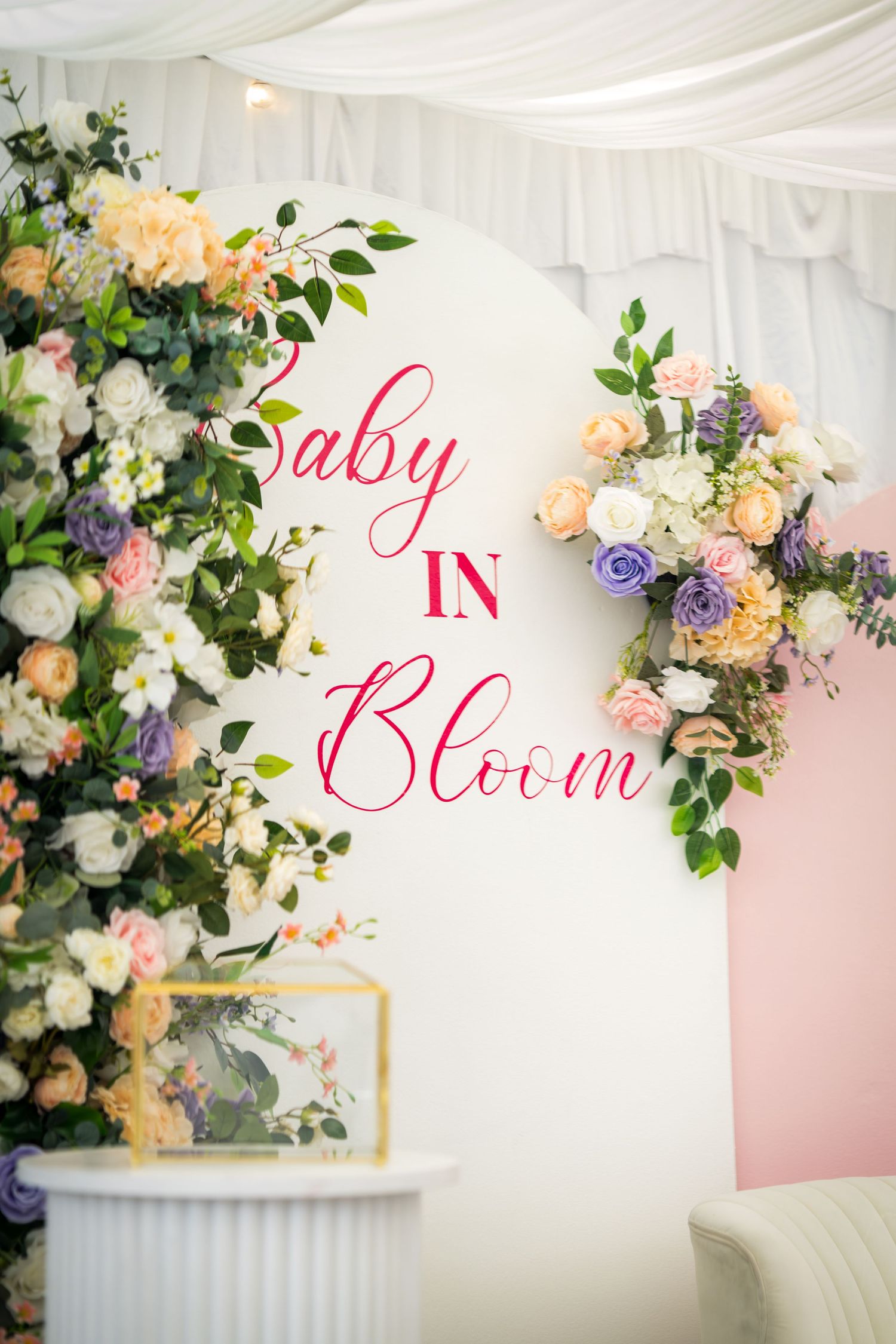 Elegant baby shower decor featuring floral arrangements and 'Baby Bloom' text against a pink and white backdrop.