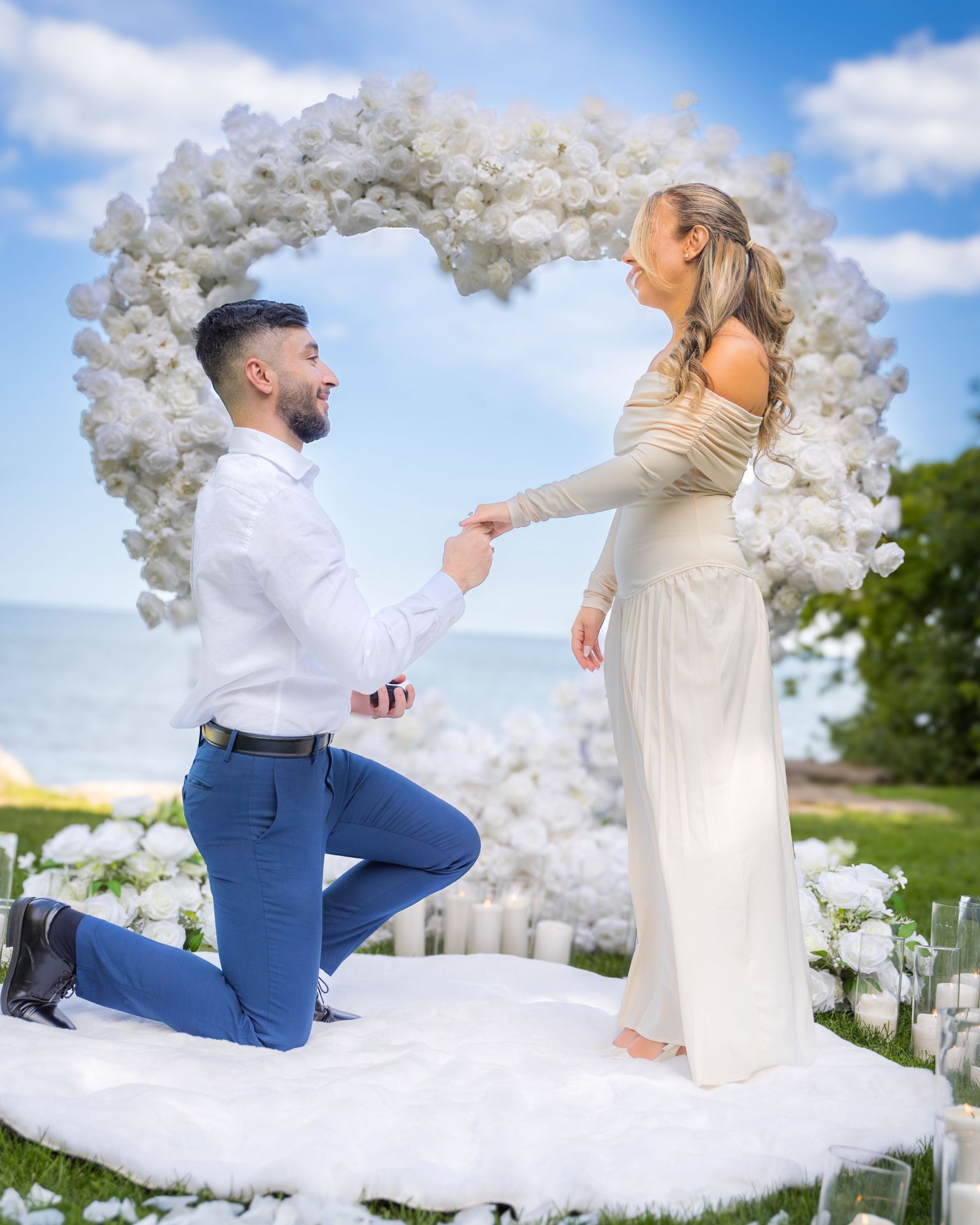 Elegant outdoor marriage proposal scene with white balloon arch and scattered rose petals.