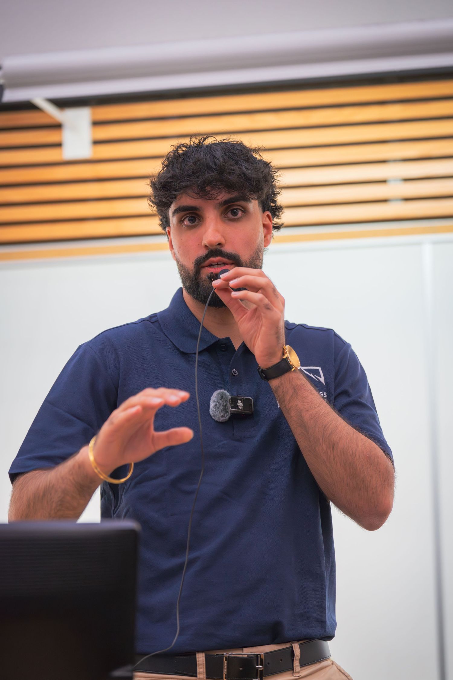 Speaker in a navy blue polo shirt gestures animatedly during a presentation.