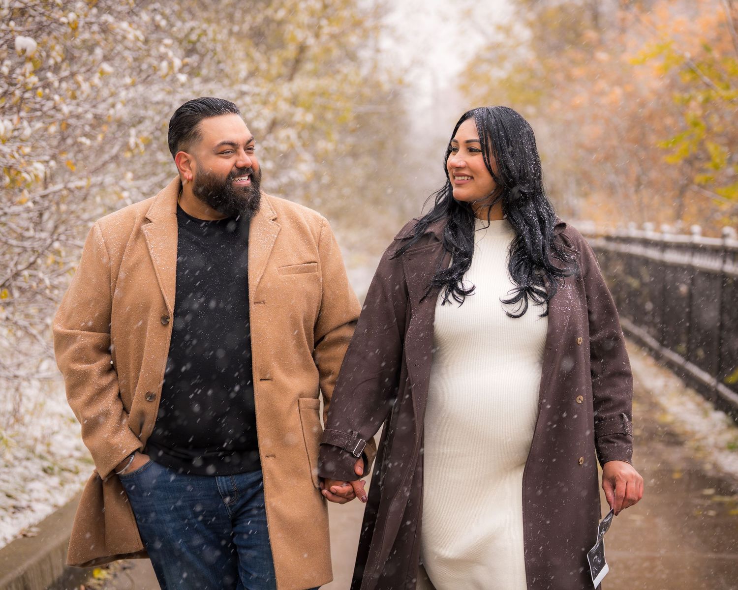 A couple shares a romantic moment outdoors during a snowy winter photoshoot while wearing warm coats.