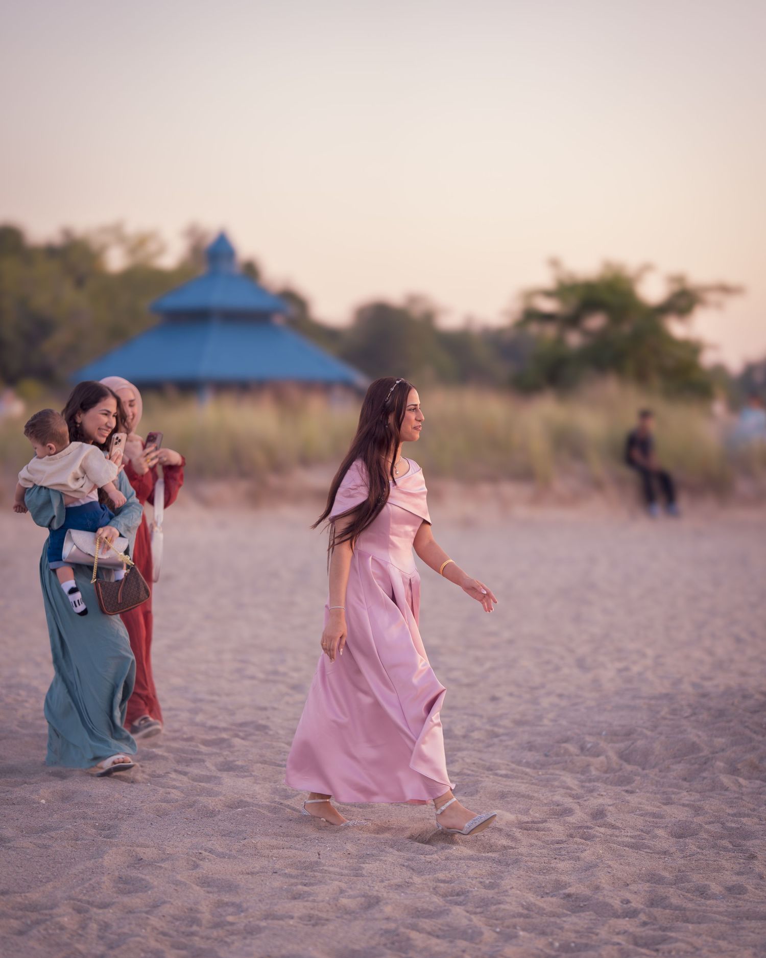 Joyful figures running and dancing on sandy beach at dusk wearing pink and blue outfits.