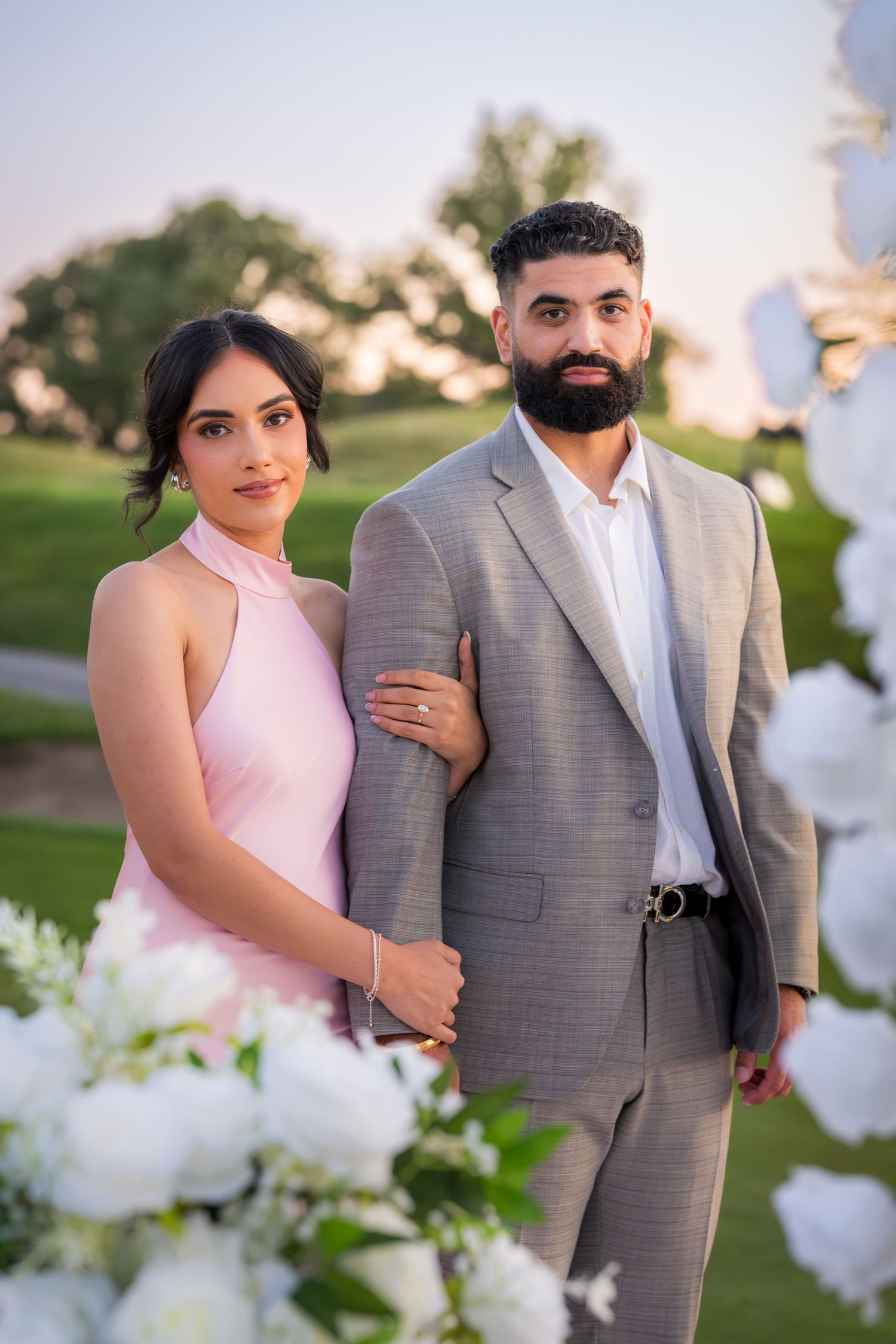 Elegant couple shares intimate moment near white floral decorations at sunset.