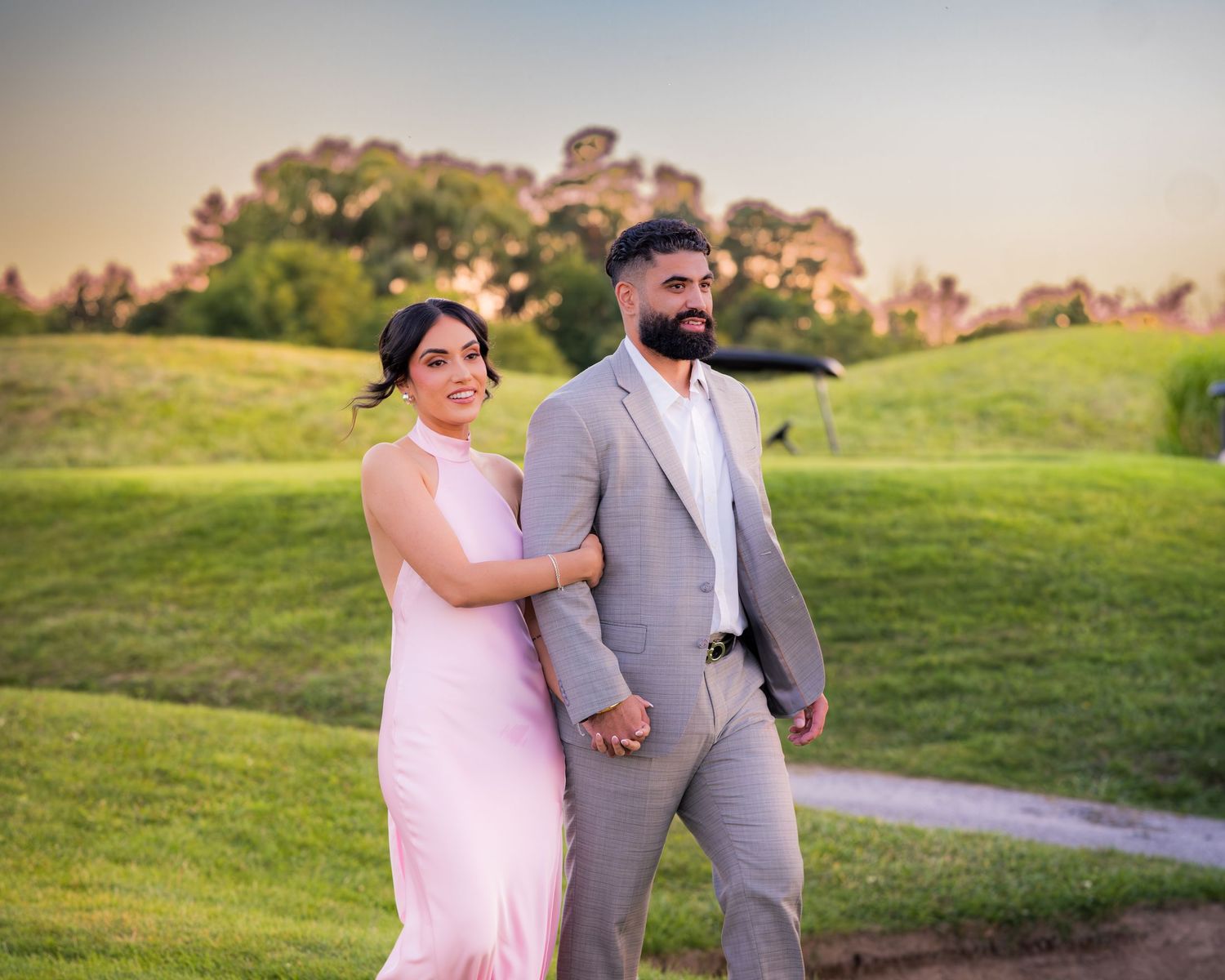Couple walking together on a grassy hill during sunset.
